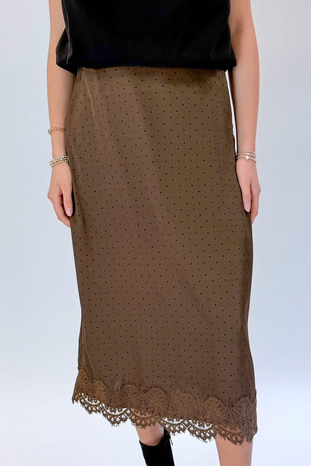 Front detail view of woman wearing Swagger Boutique’s Brown Polka Dot Lace Lined Satin Skirt by Entro with Black Satin Cowlneck Sleeveless Top against white studio background.