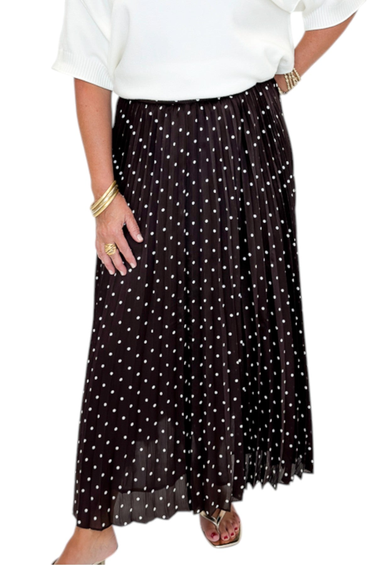 Front detail view of woman wearing Swagger Boutique’s Brown Polka Dot Pleated Skirt with top against white studio background.