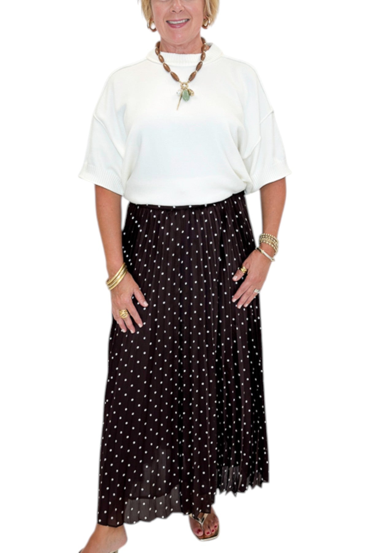 Front detail view of woman wearing Swagger Boutique’s Brown Polka Dot Pleated Skirt with top against white studio background.