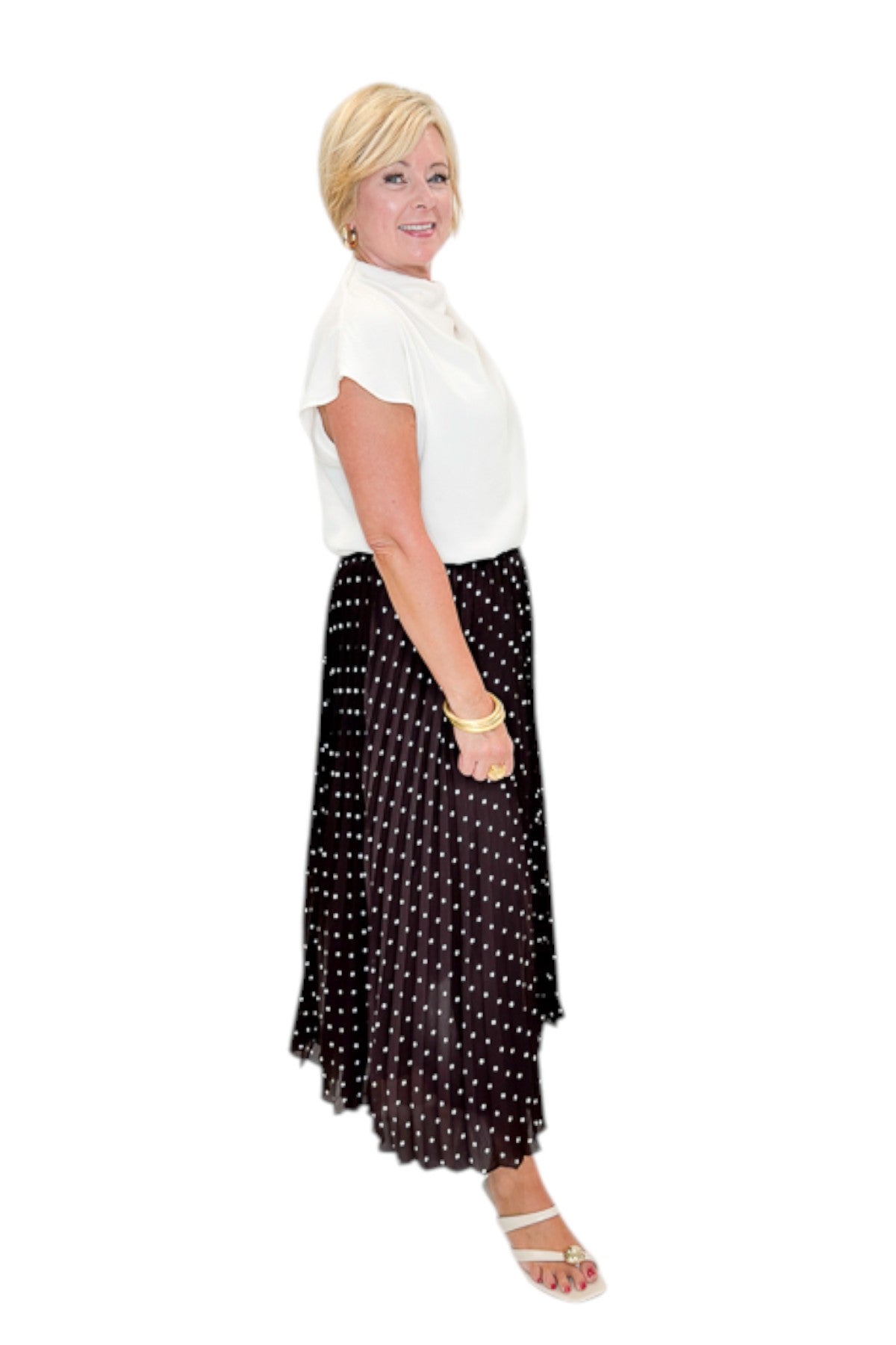 Side view of woman wearing Swagger Boutique’s Brown Polka Dot Pleated Skirt with top against white studio background.