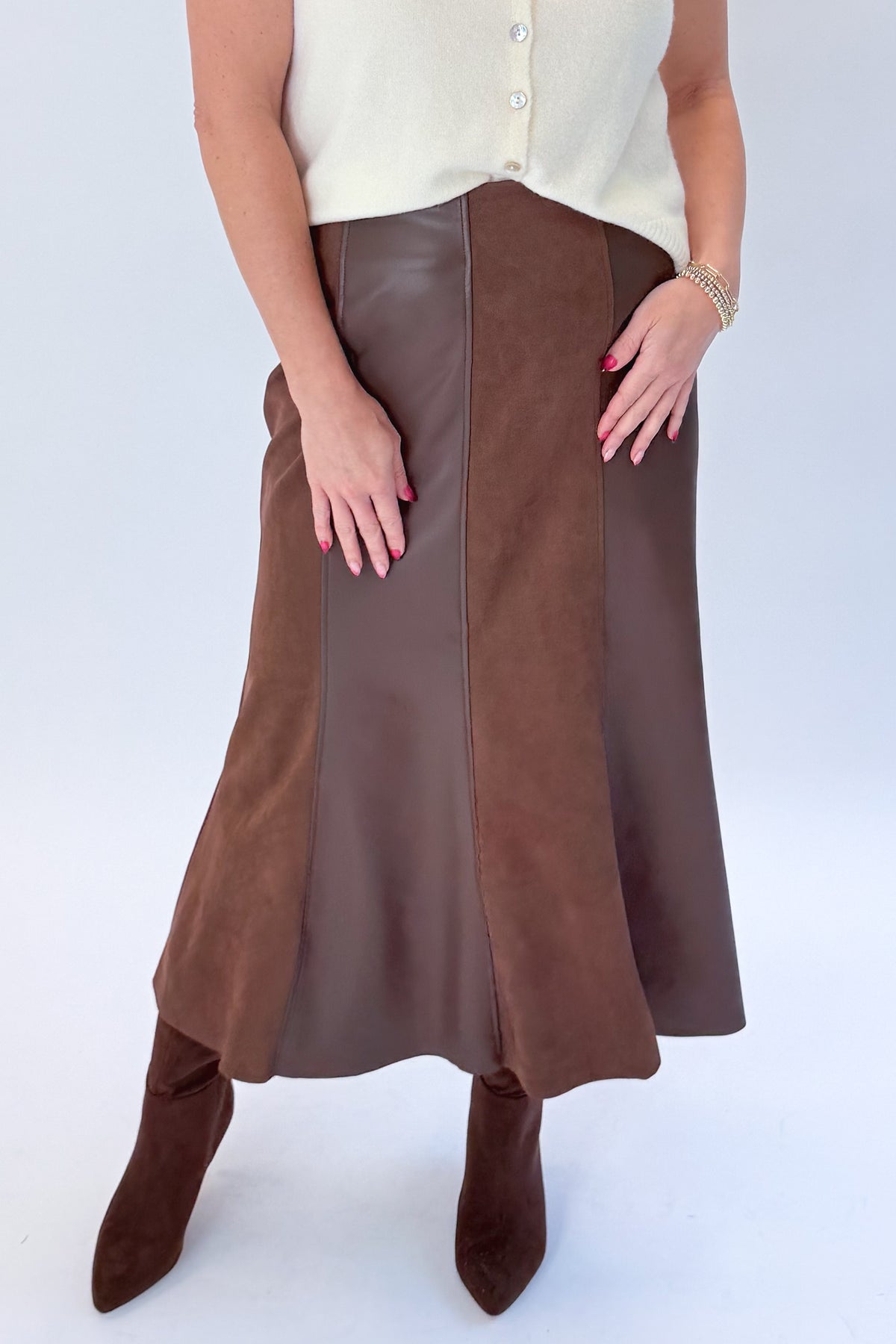 Front detail view of woman wearing Swagger Boutique’s Cream Sleeveless Button Up Sweater with Brown Suede & Leather Midi Skirt by THML against white studio background.