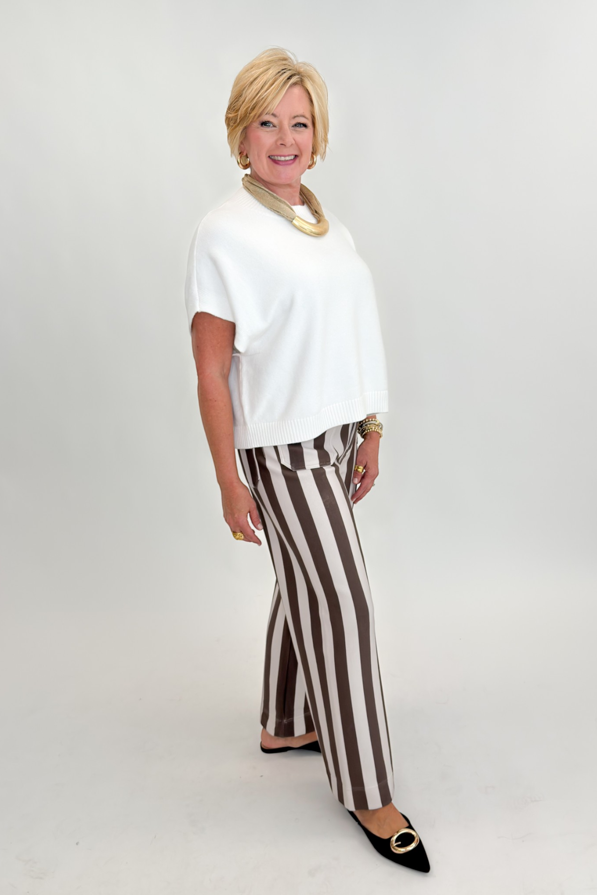 Side view of woman wearing Swagger Boutique’s sweater with Brown & Beige Striped Pants by Entro against white studio background.