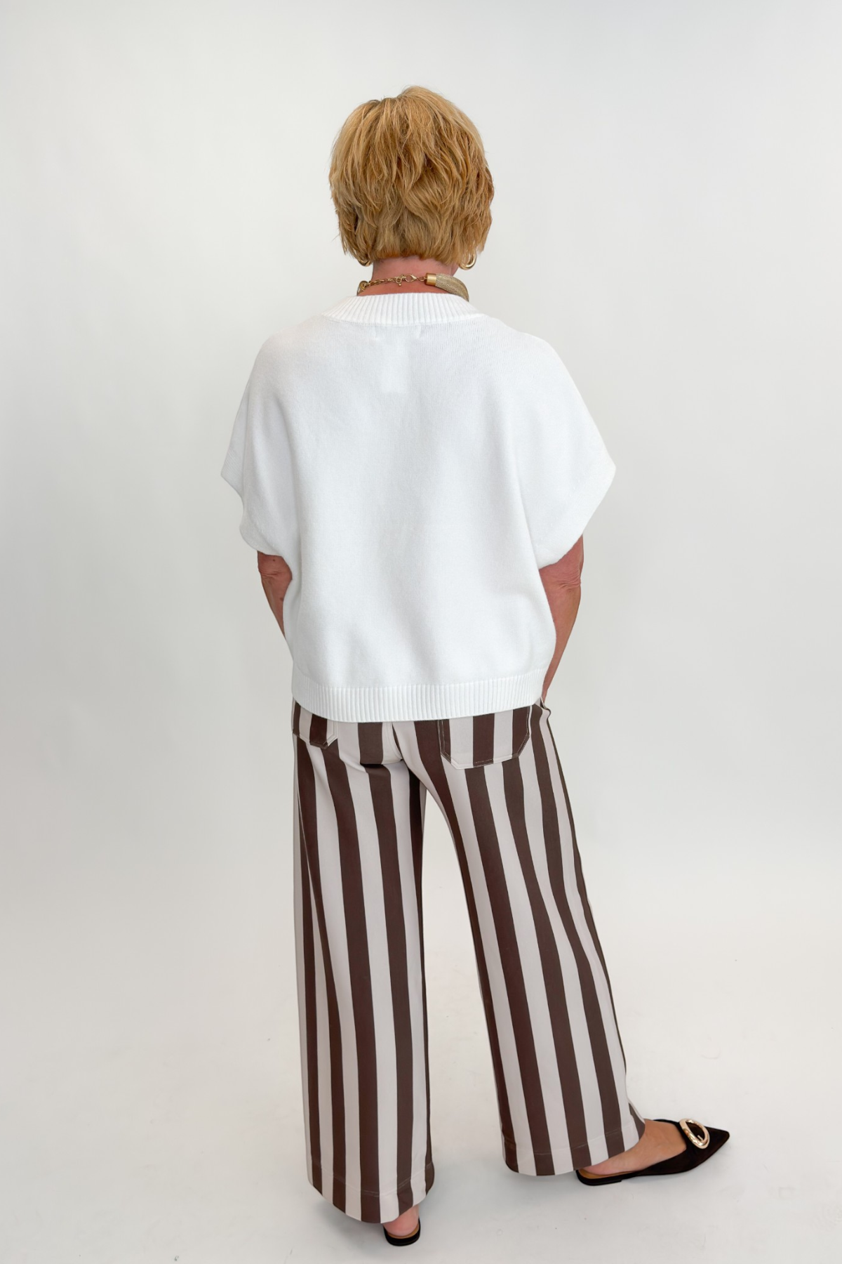 Back view of woman wearing Swagger Boutique’s sweater with Brown & Beige Striped Pants by Entro against white studio background.