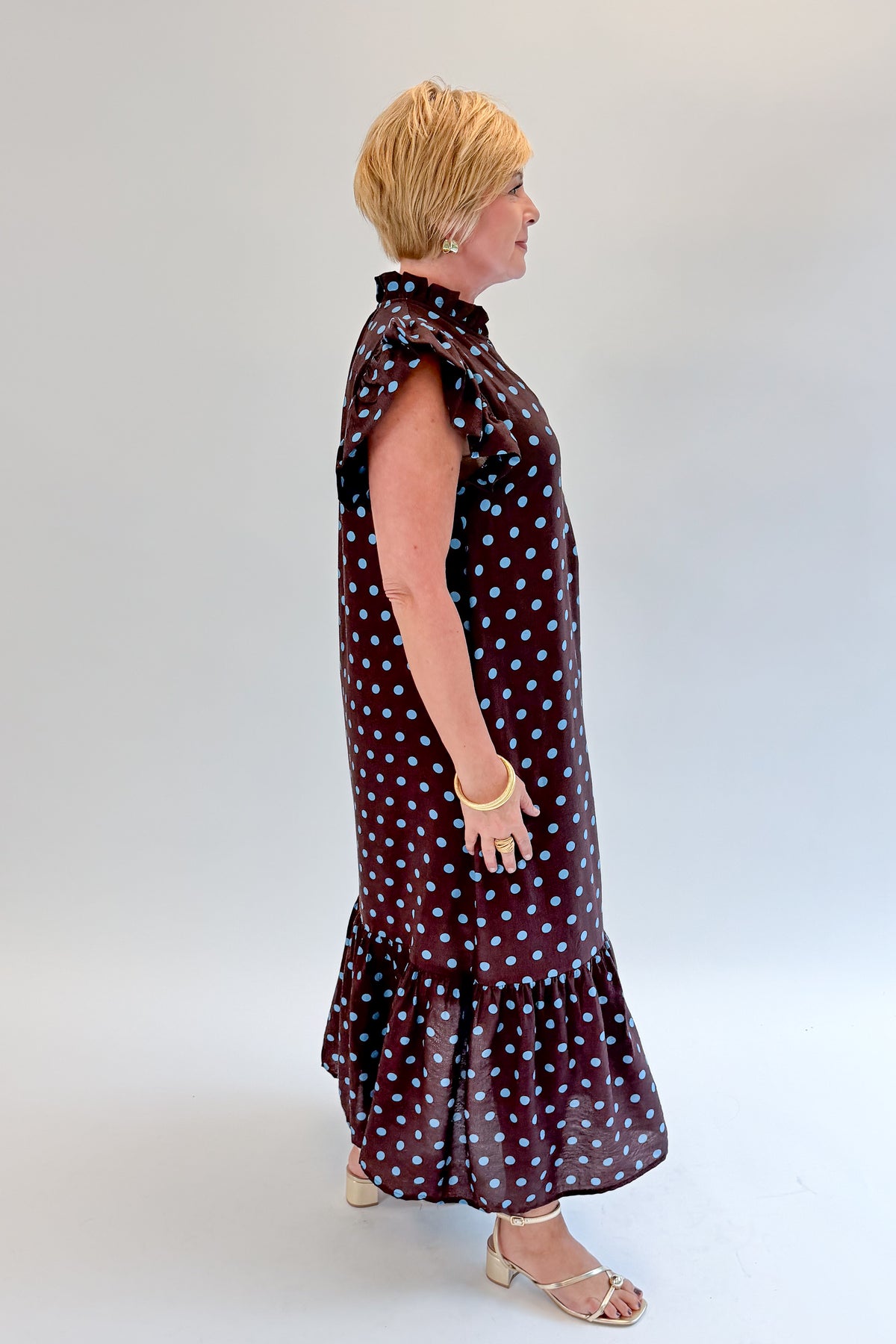 Side view of woman wearing Swagger Boutique’s Brown & Blue Polka Dot Midi Dress by Entro with heels against white studio background.