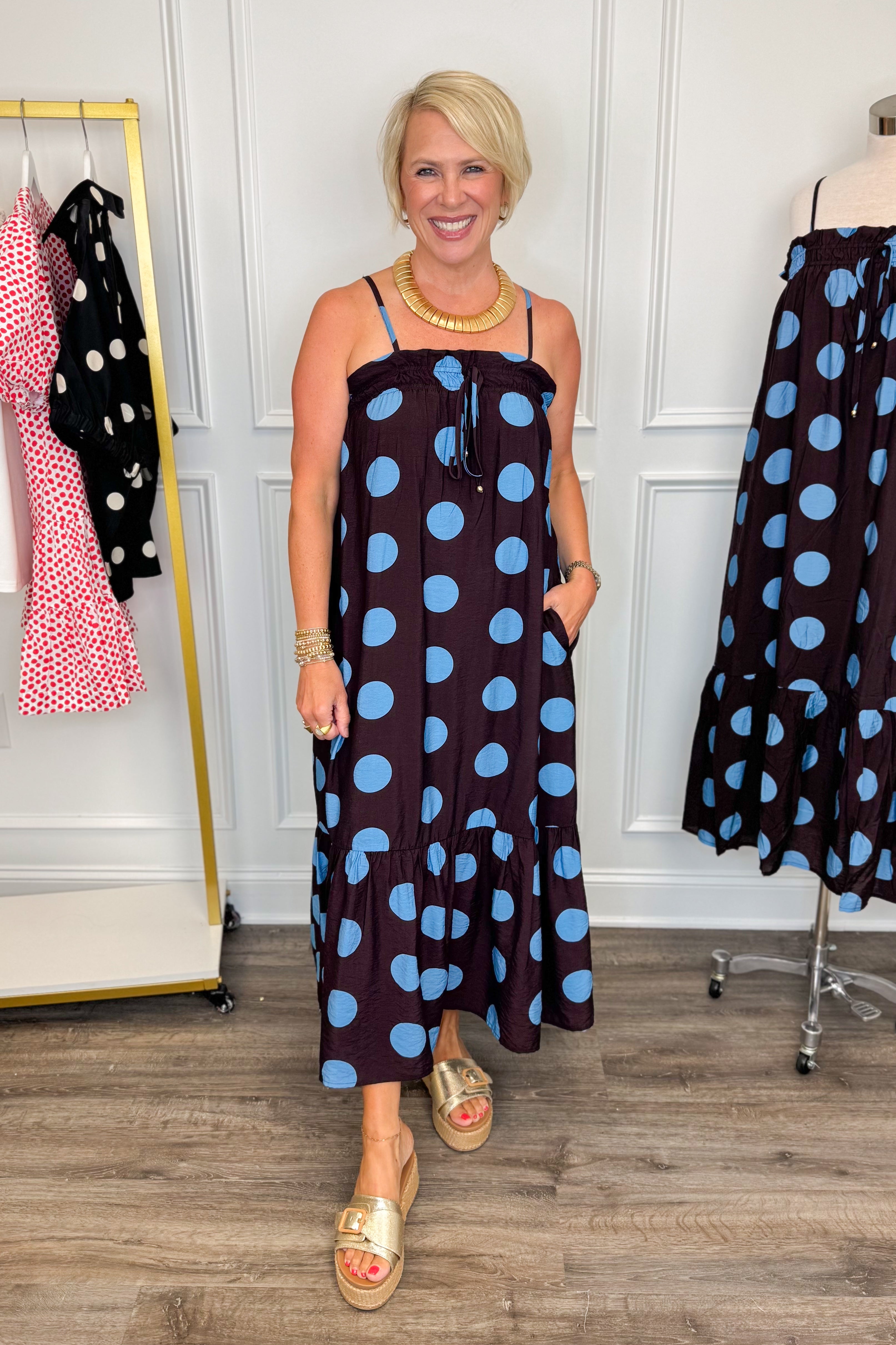 Front view of woman wearing Swagger Boutiqueās Works Every Time Brown & Blue Polka Dot Midi Dress by Entro with clothing hanging in the background.