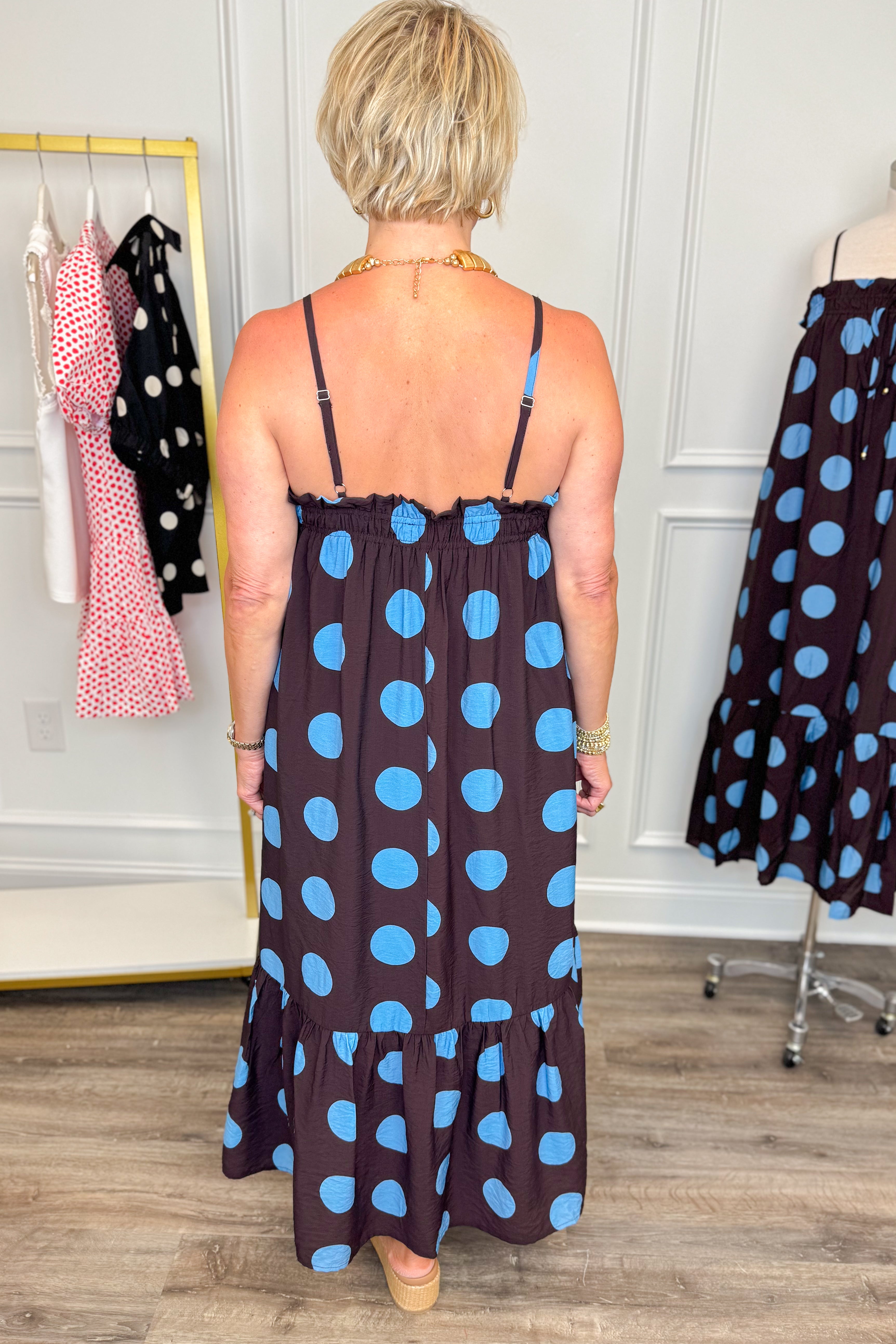 Back view of woman wearing Swagger Boutiqueās Works Every Time Brown & Blue Polka Dot Midi Dress by Entro with clothing hanging in the background.