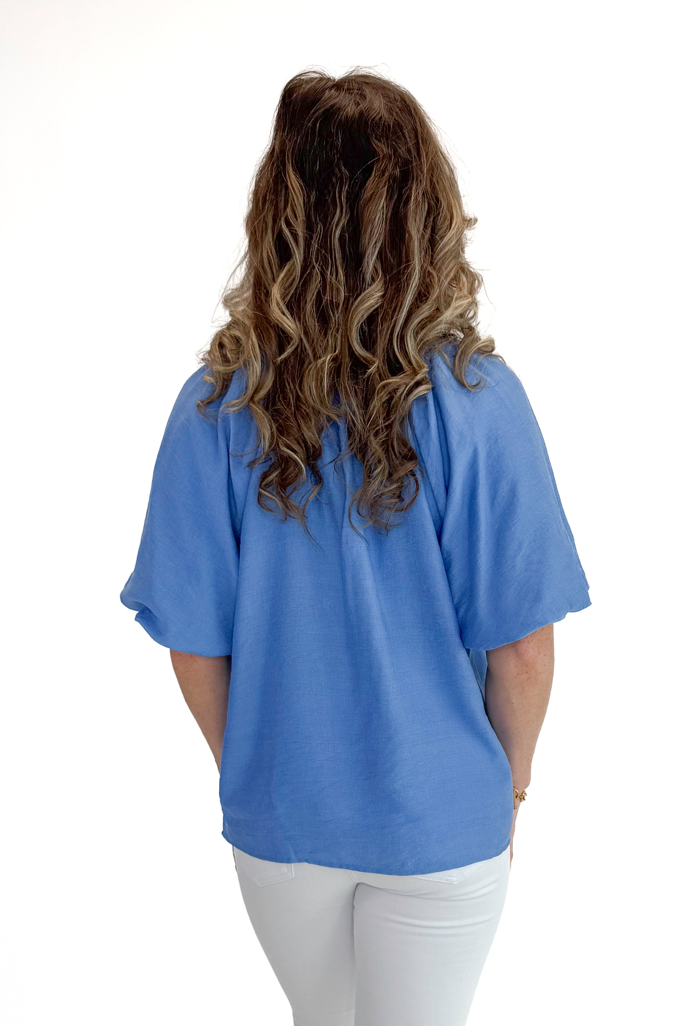 Back view of woman wearing Blue Floral Embroidered Top with jeans against white studio background.