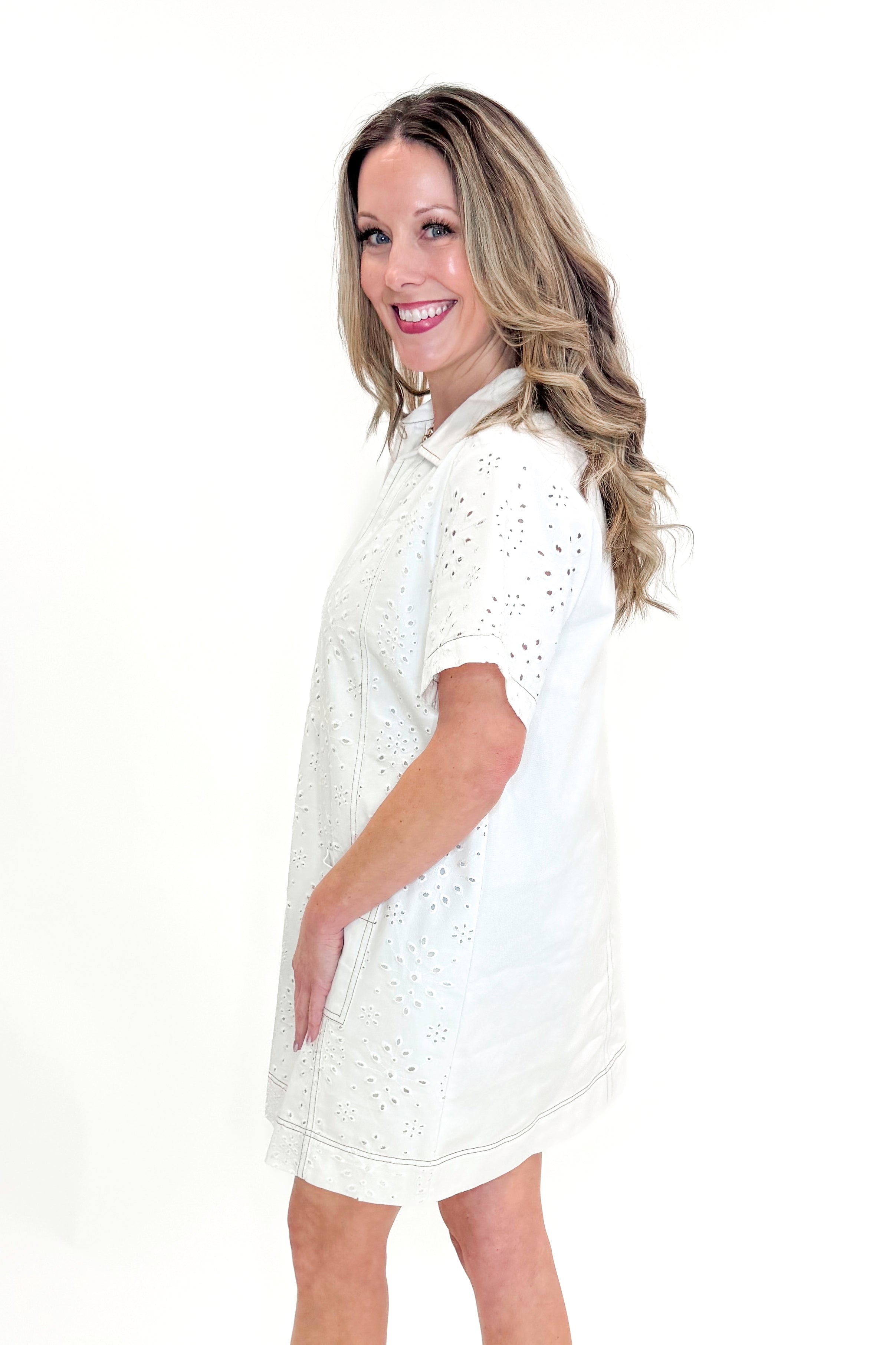 Side view of woman wearing Cream Eyelet Pocket Detail Dress with sandals against white studio background.