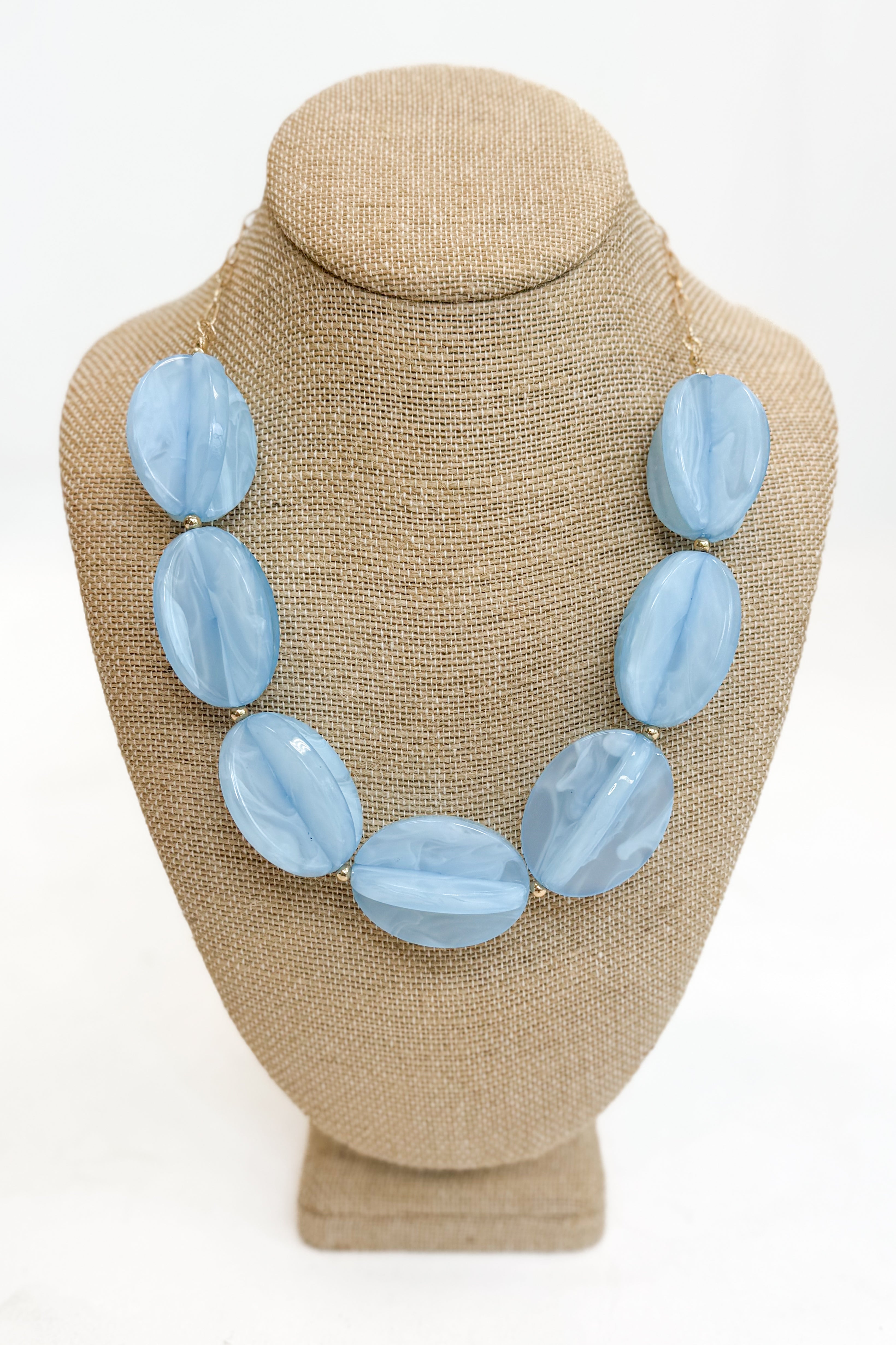 Blue necklace on a beige mannequin bust against a white background