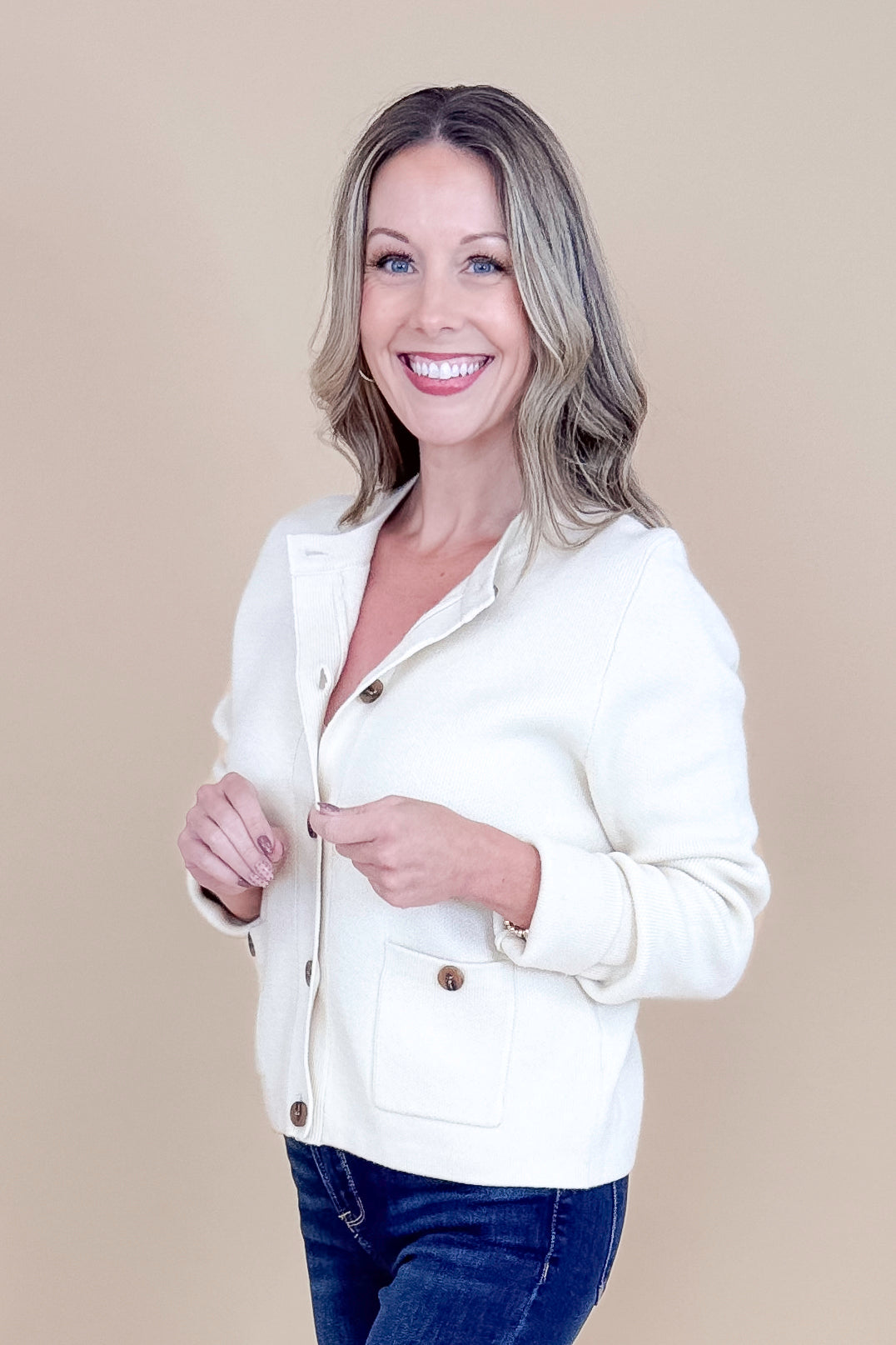 Side view of woman wearing Oatmeal Button Detail Cardigan with jeans against tan studio background.