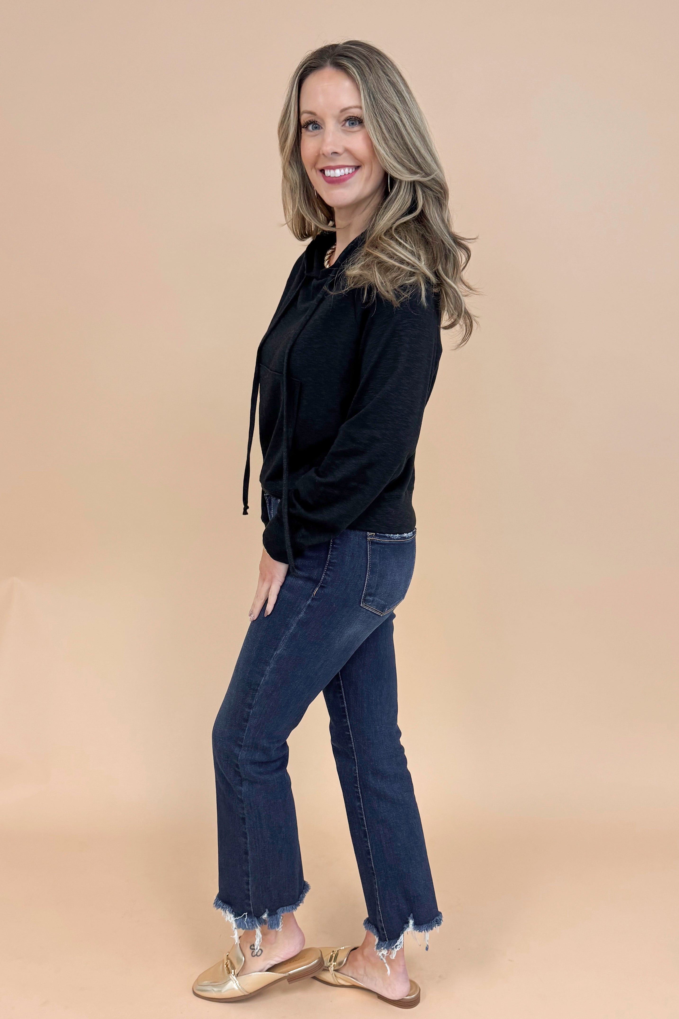 Side view of woman wearing Black Hooded Sweatshirt and jeans with a tan background.