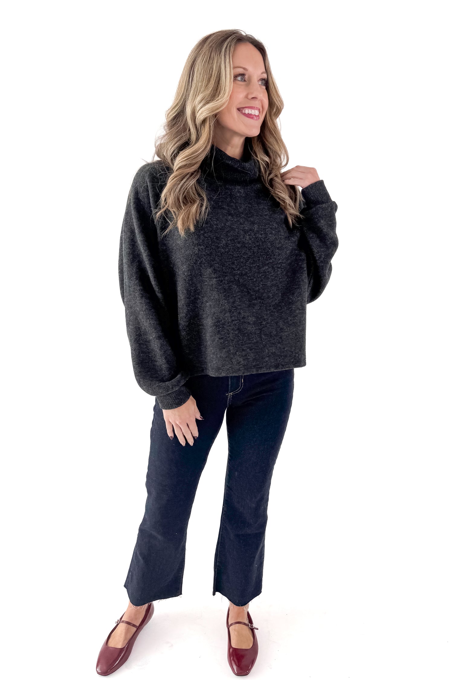 Front view of woman wearing charcoal sweater with jeans against white studio background.