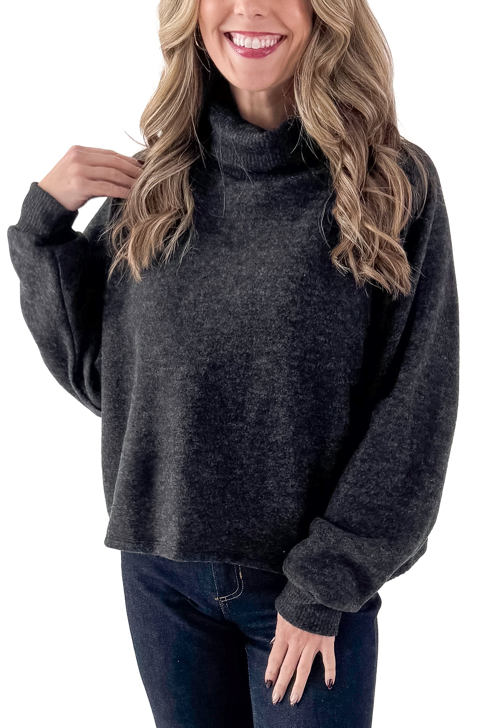Front view of woman wearing charcoal sweater with jeans against white studio background.