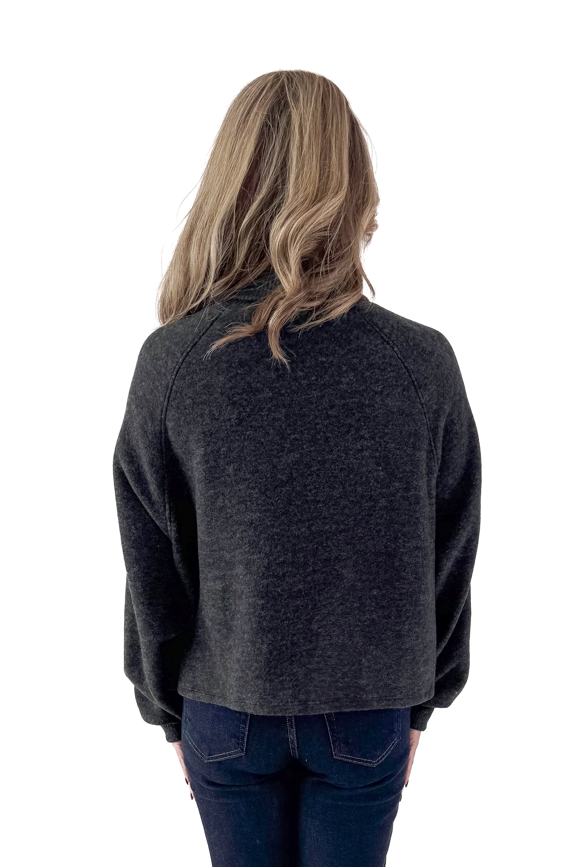 Back view of woman wearing charcoal sweater with jeans against white studio background.
