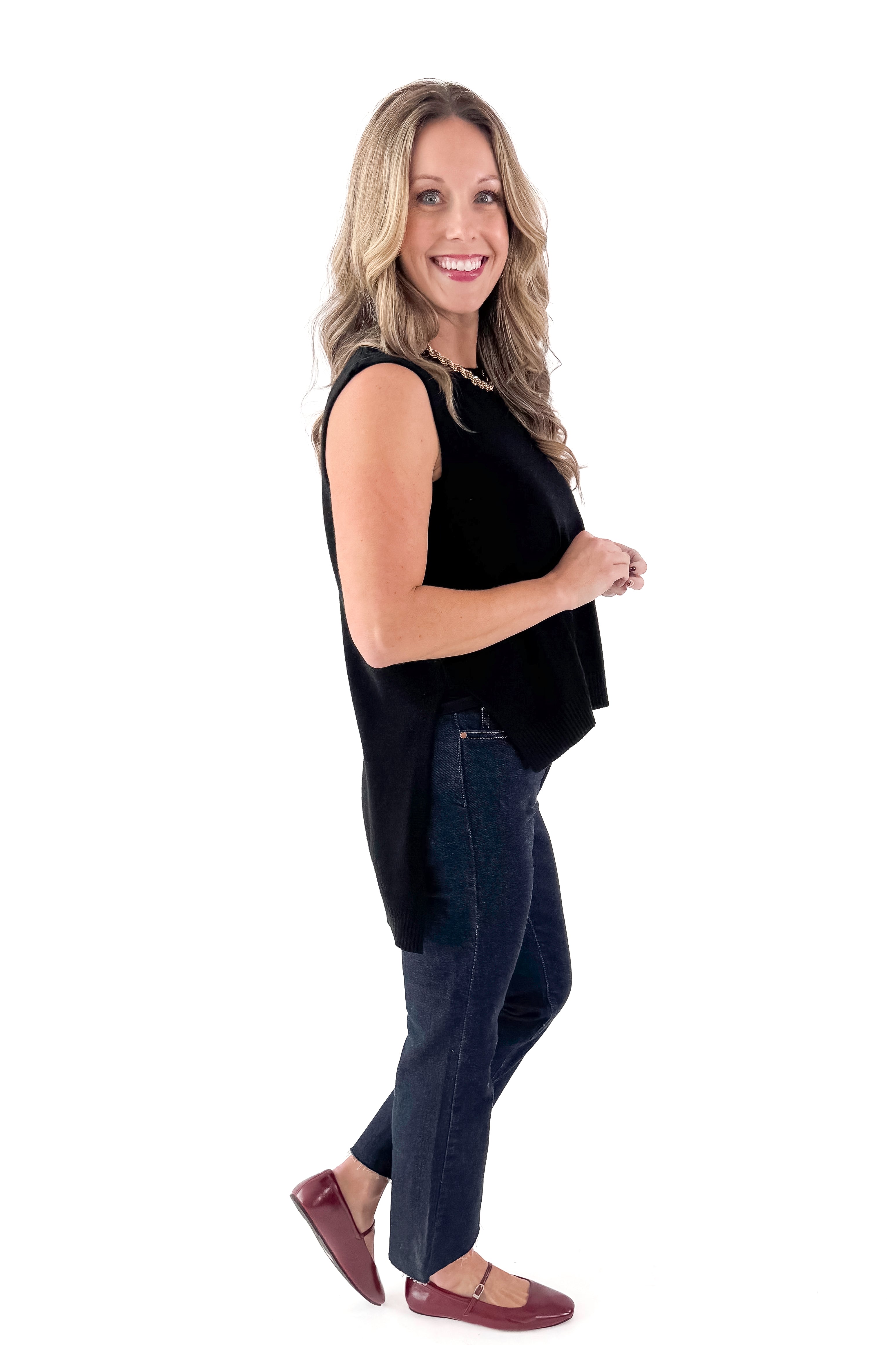 Side view of woman wearing black sweater with jeans against white studio background.