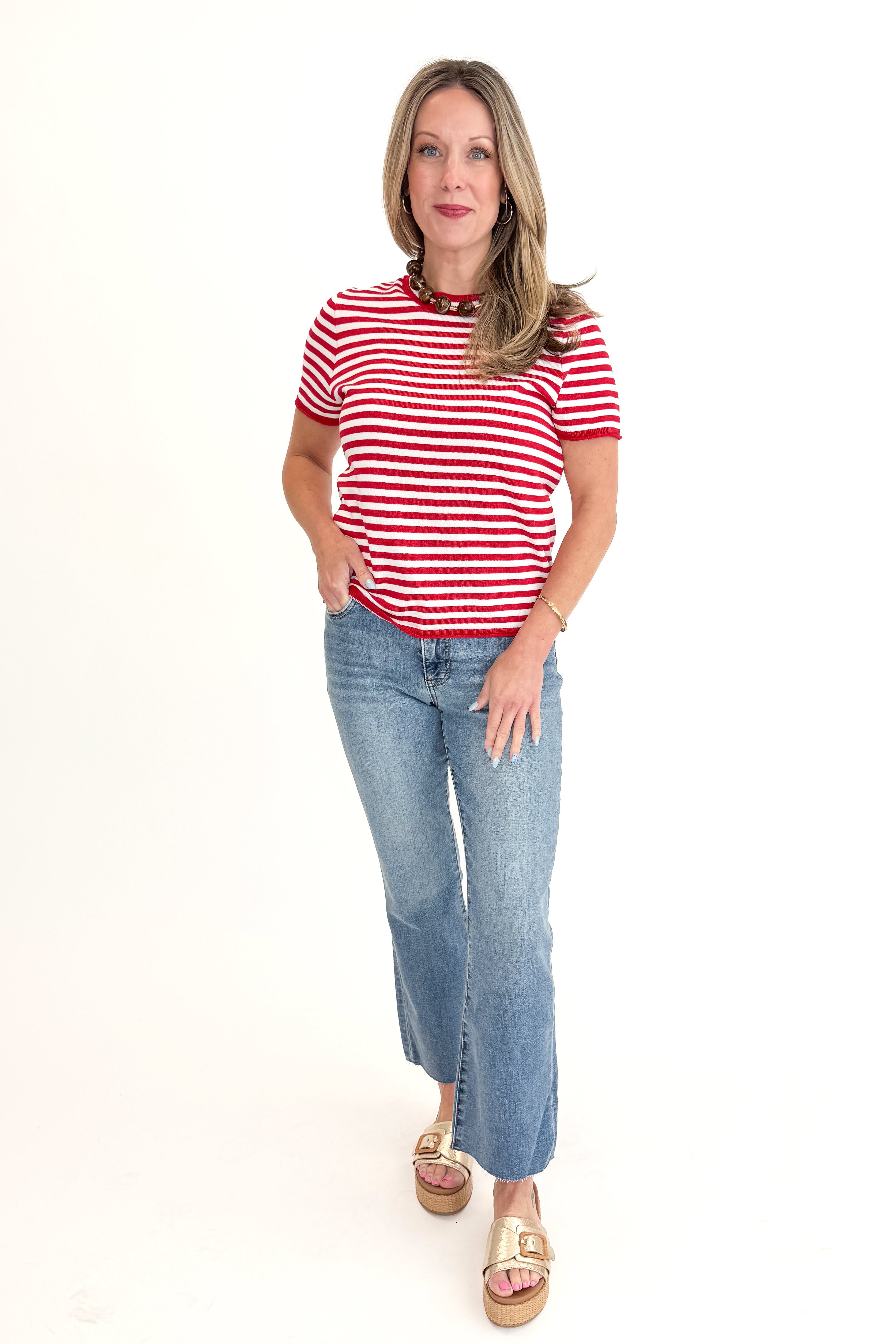 Front view of woman wearing Red & White Striped Short Sleeve Sweater with jeans against white studio background.