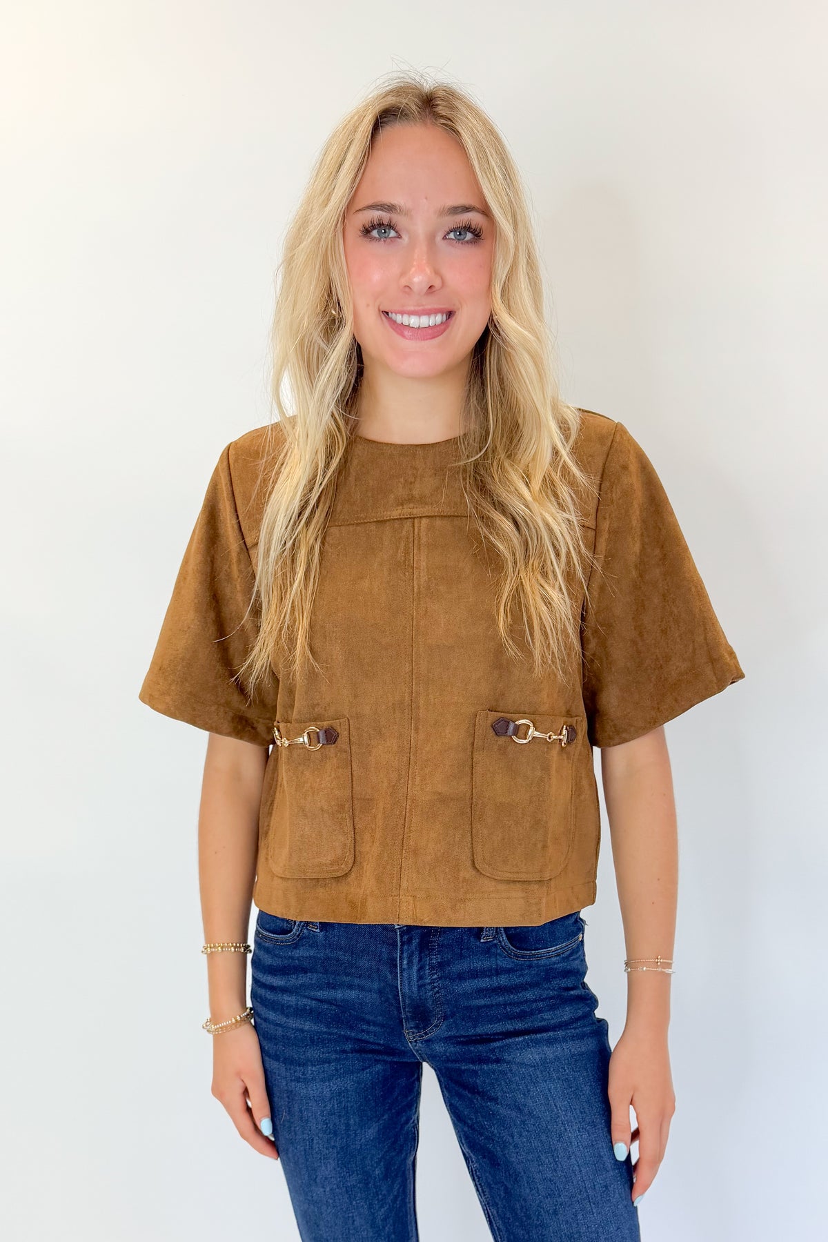 Front view of woman wearing Swagger Boutique’s Camel Suede Horsebit Pocket Top by Entro with jeans against white studio background.