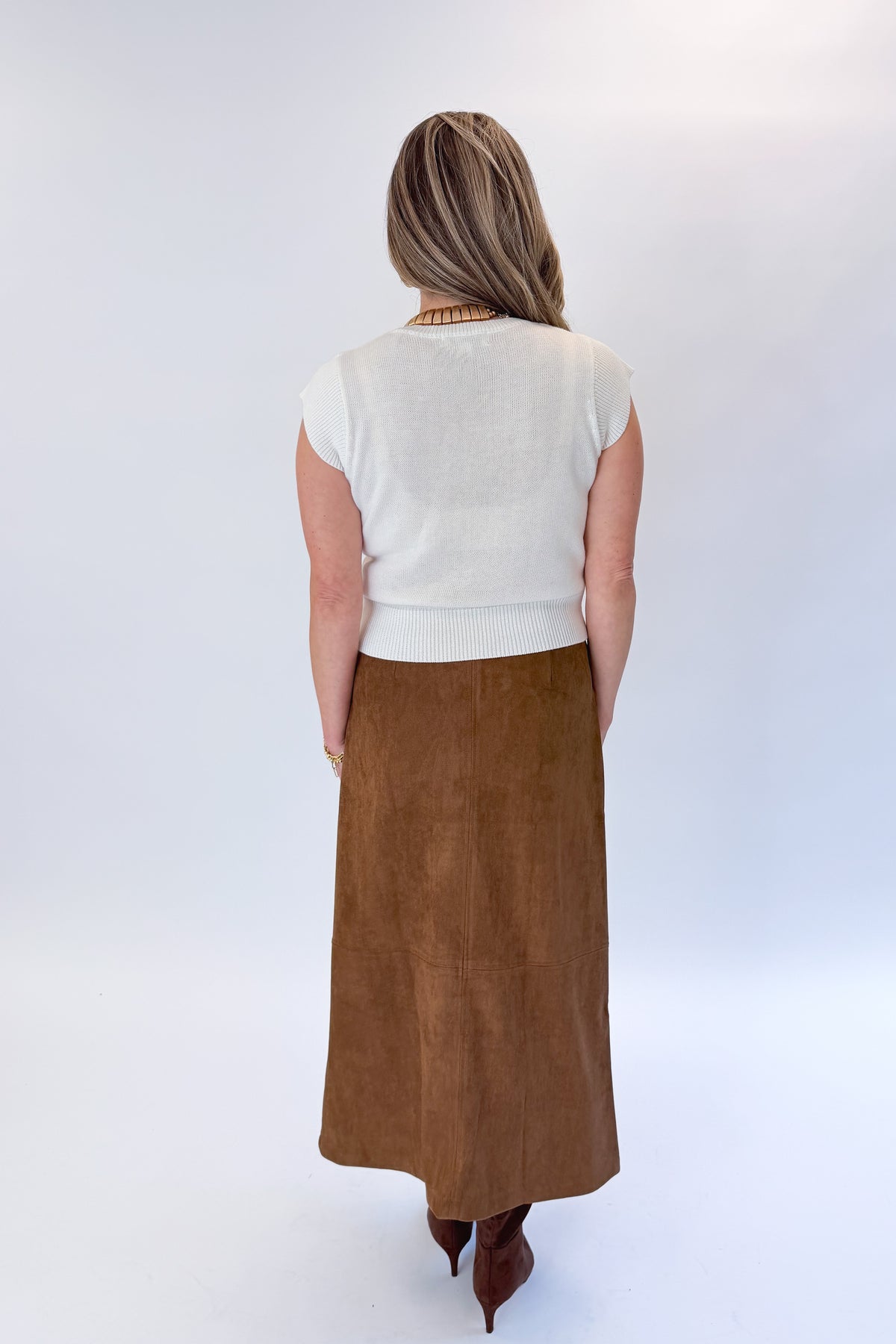Back view of woman wearing Swagger Boutique’s White Cap Sleeve Sweater by PINCH with Camel Suede Midi Skirt With Pockets by Entro against white studio background.