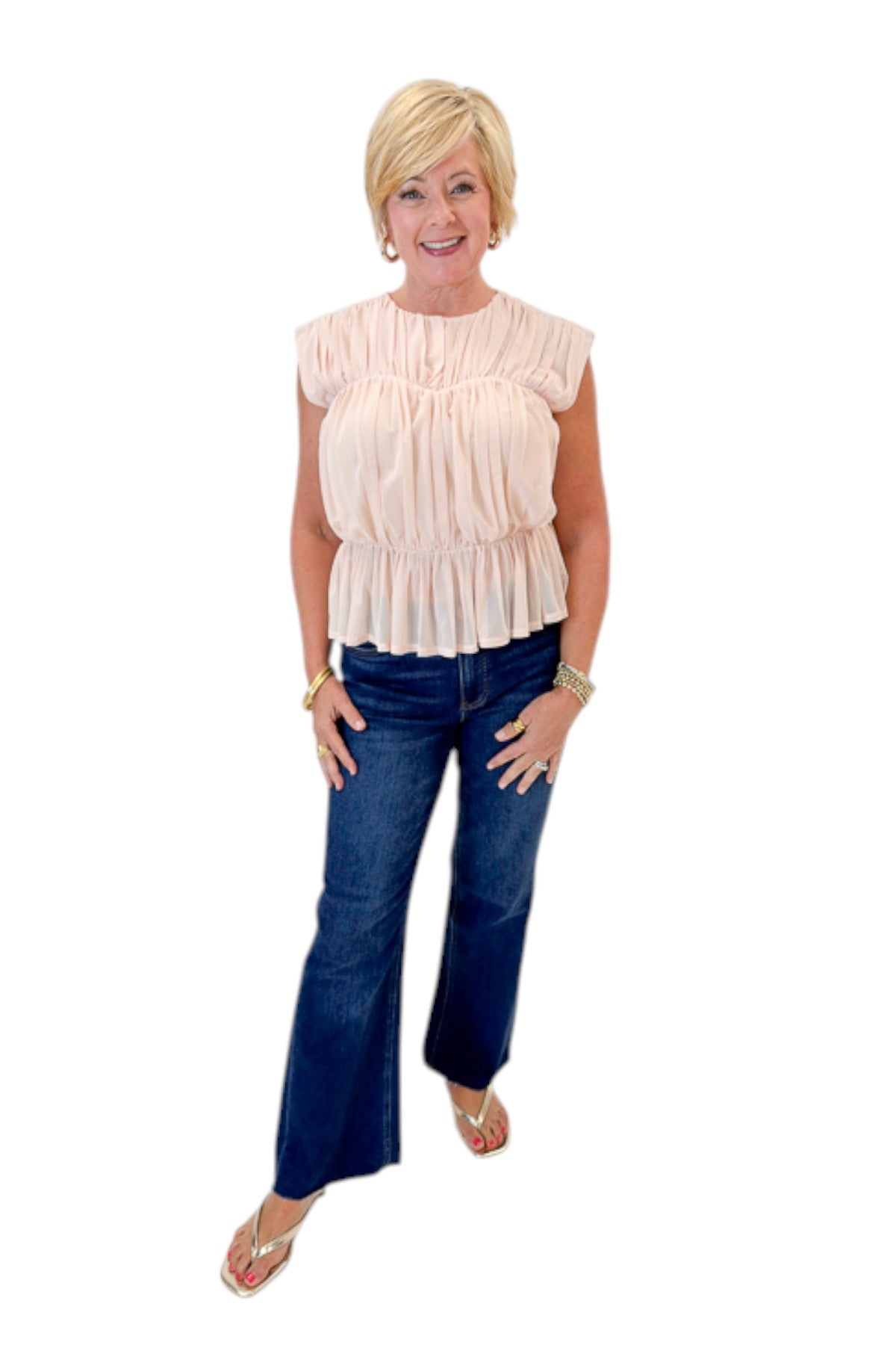 Front view of woman wearing Swagger Boutique’s Champagne Shirred Peplum Top with jeans against white studio background.