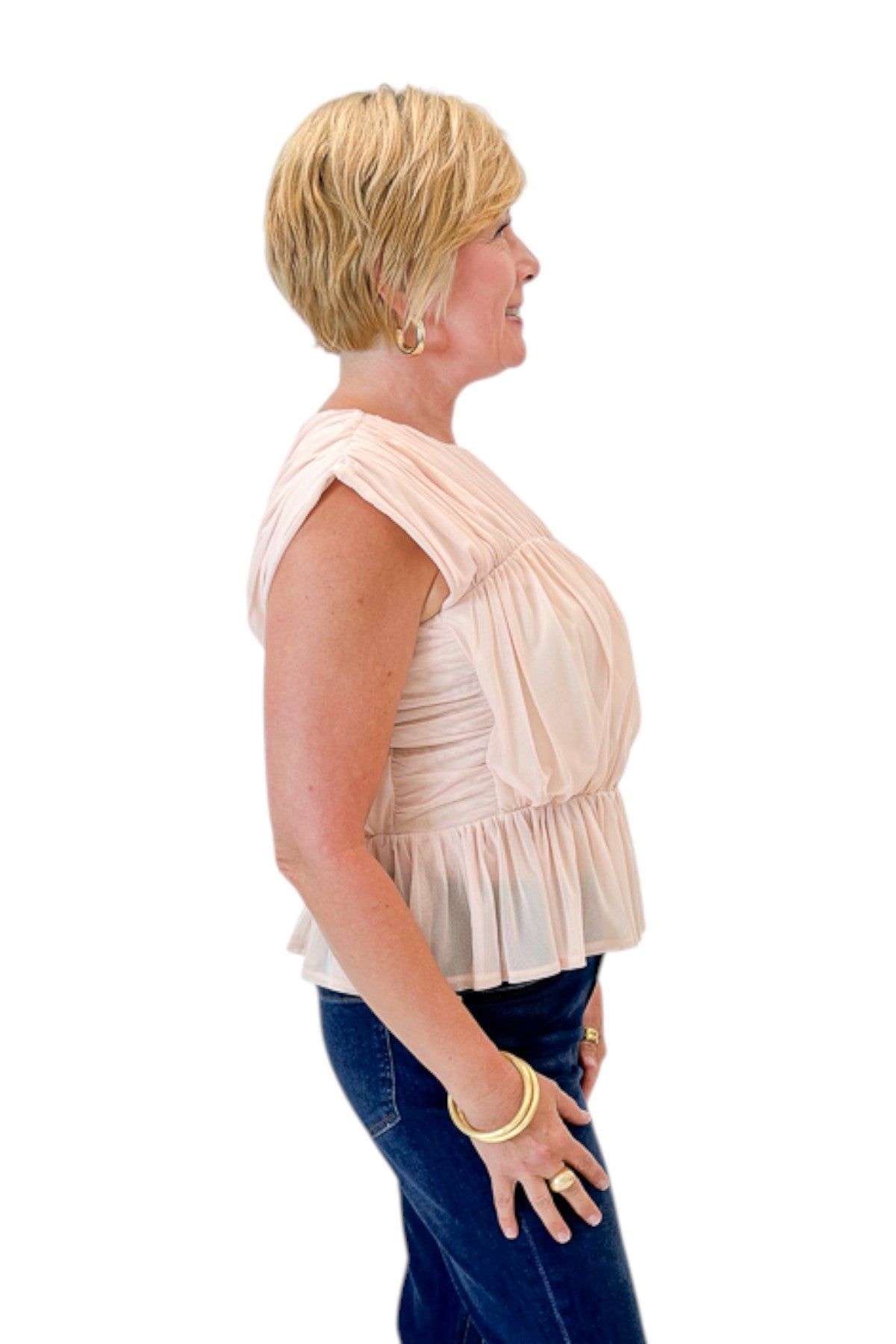 Side view of woman wearing Swagger Boutique’s Champagne Shirred Peplum Top with jeans against white studio background.
