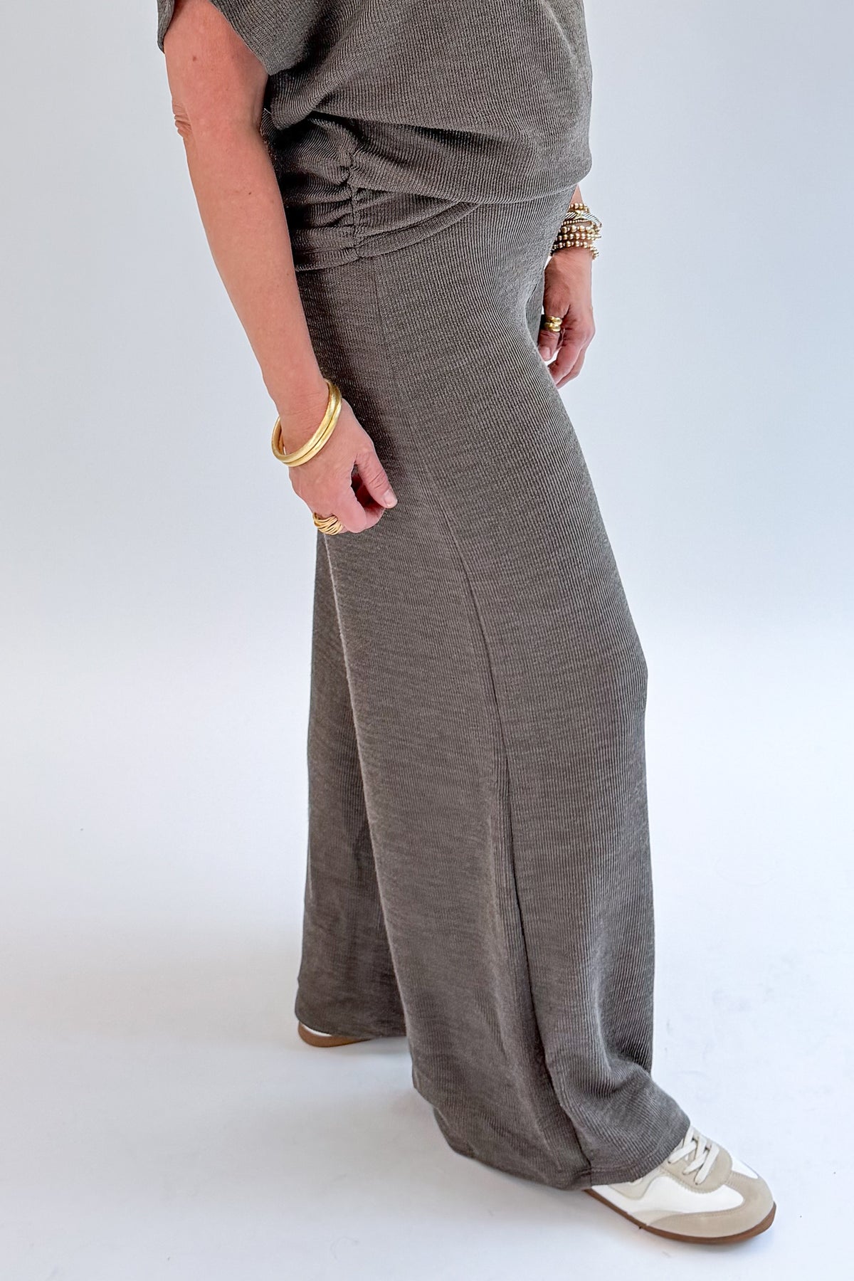 Side detail view of woman wearing Swagger Boutique’s Charcoal Ribbed Short Sleeve Turtleneck Top & Lounge Pants against white studio background.