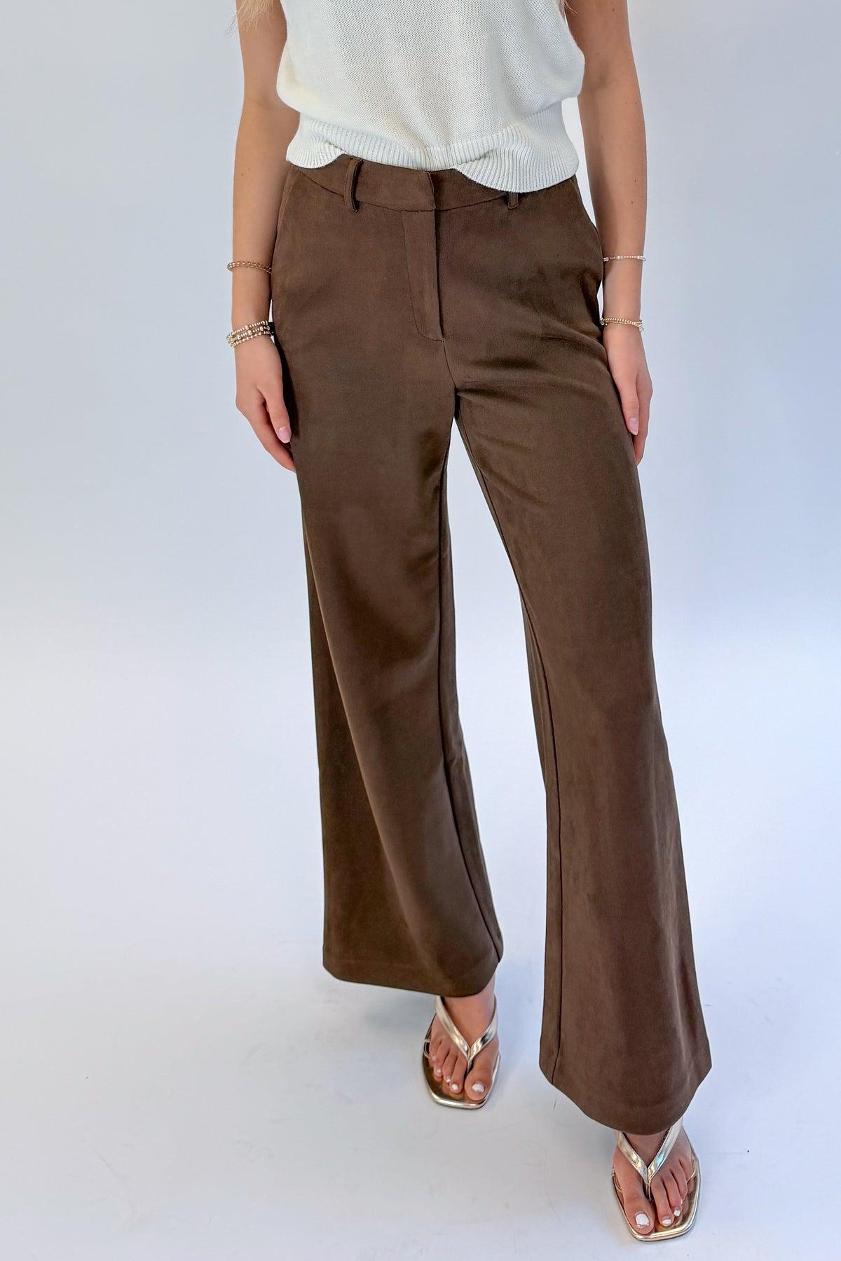 Front view of woman wearing Swagger Boutique’s Chocolate Brown Suede Pants with Living My Best Life White Cap Sleeve Sweater by PINCH against white studio background.