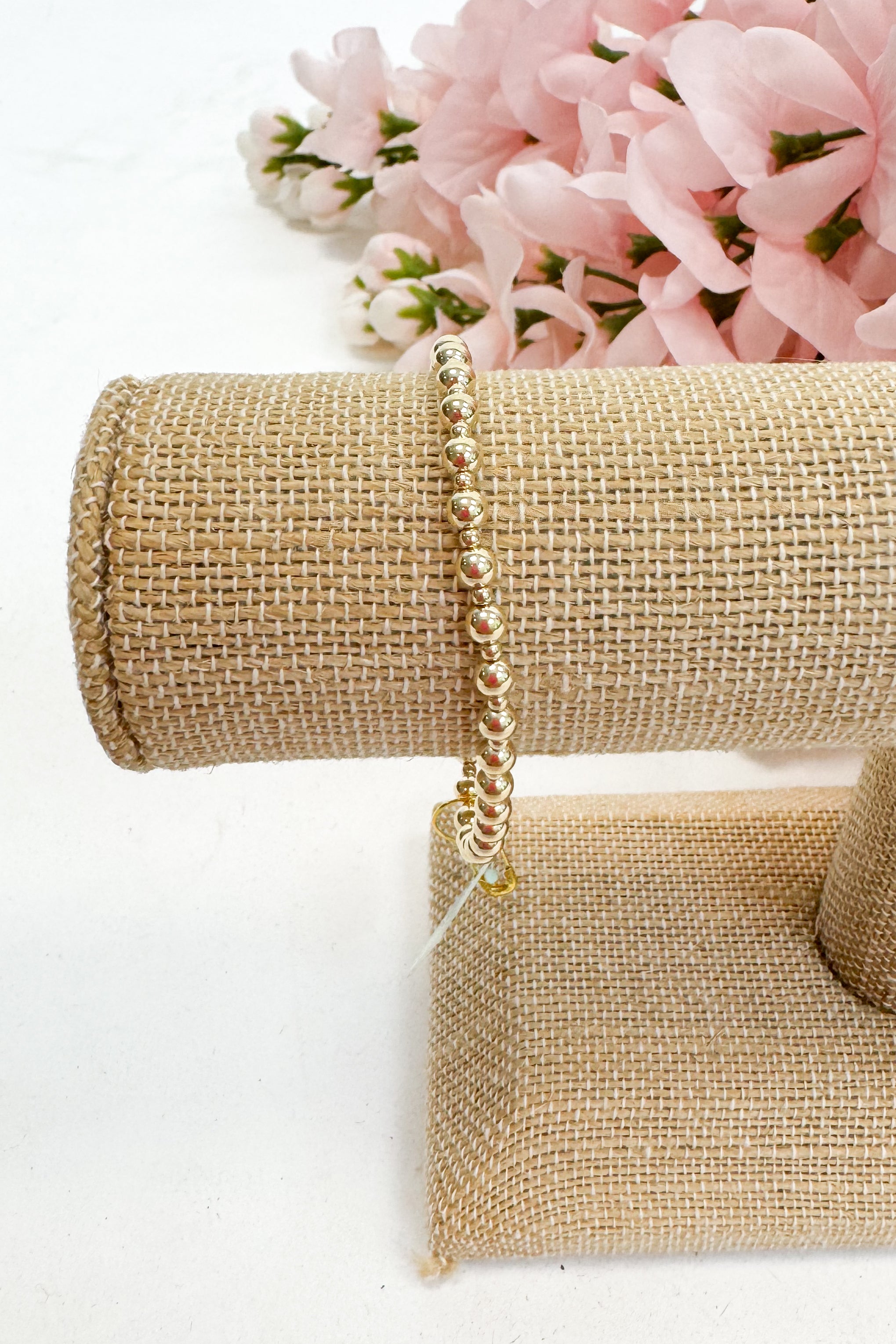 Gold bracelet on a gold jewelry stand with pink flowers in the background
