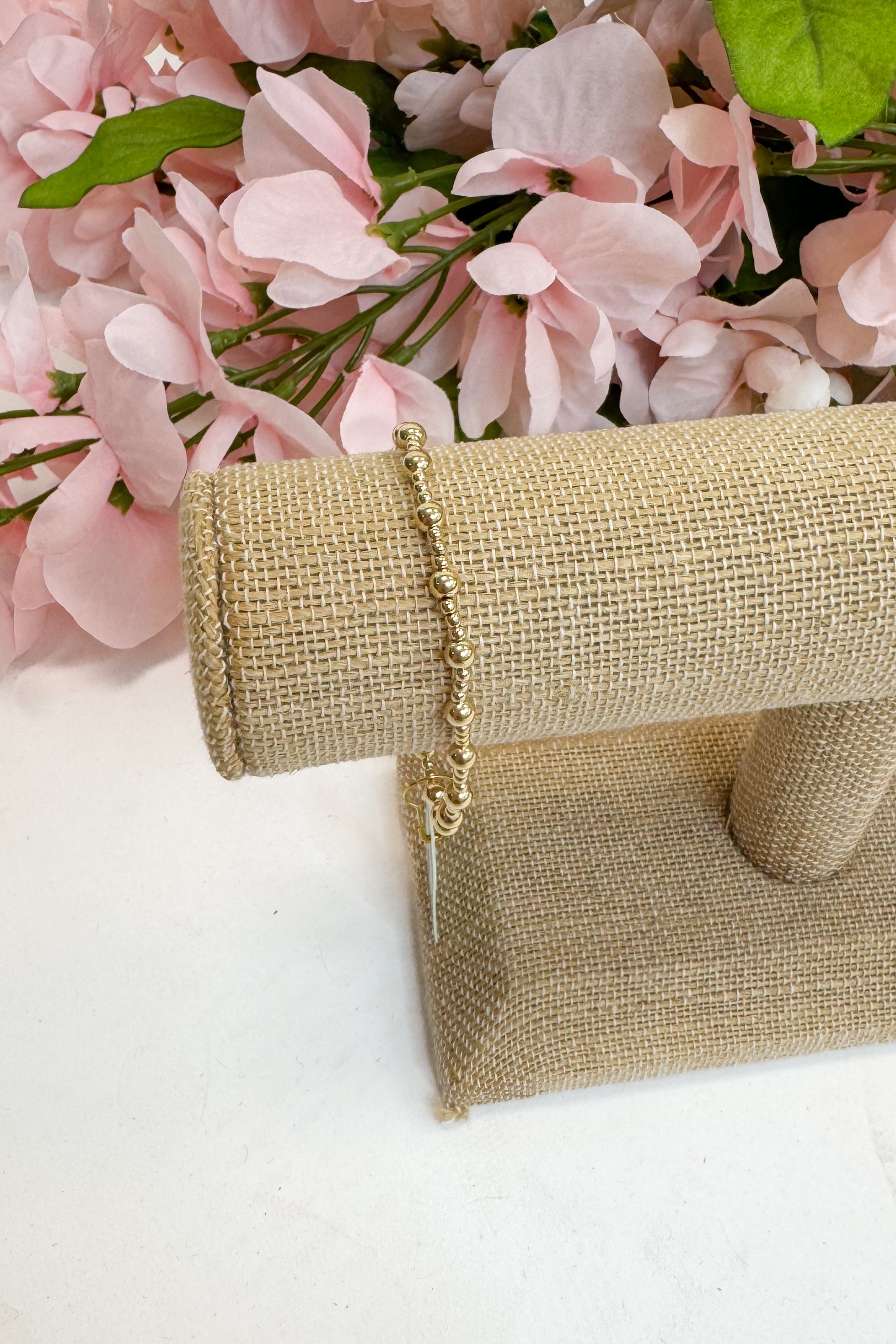 Gold bracelet on a burlap roll with pink flowers in the background