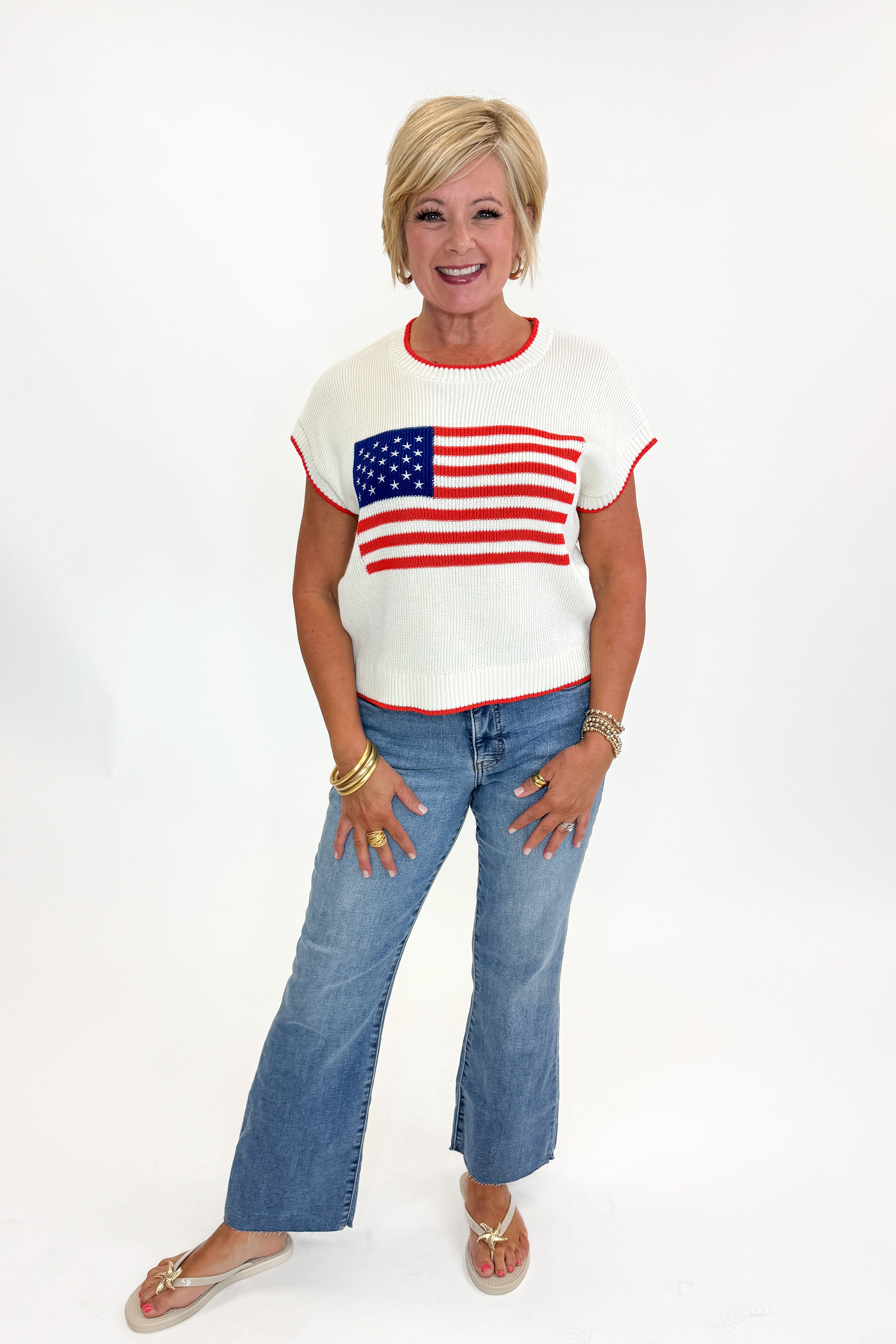 Front view of woman wearing Swagger Boutiqueās Sleeveless Patriot Sweater In Cloud by Z Supply with jeans and sandals against white studio background.