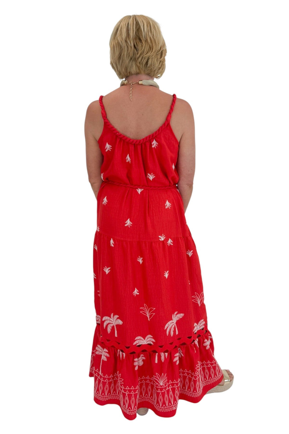 Back view of woman wearing Swagger Boutiqueās Coral Palm Embroidered Maxi Dress with sandals against white studio background.