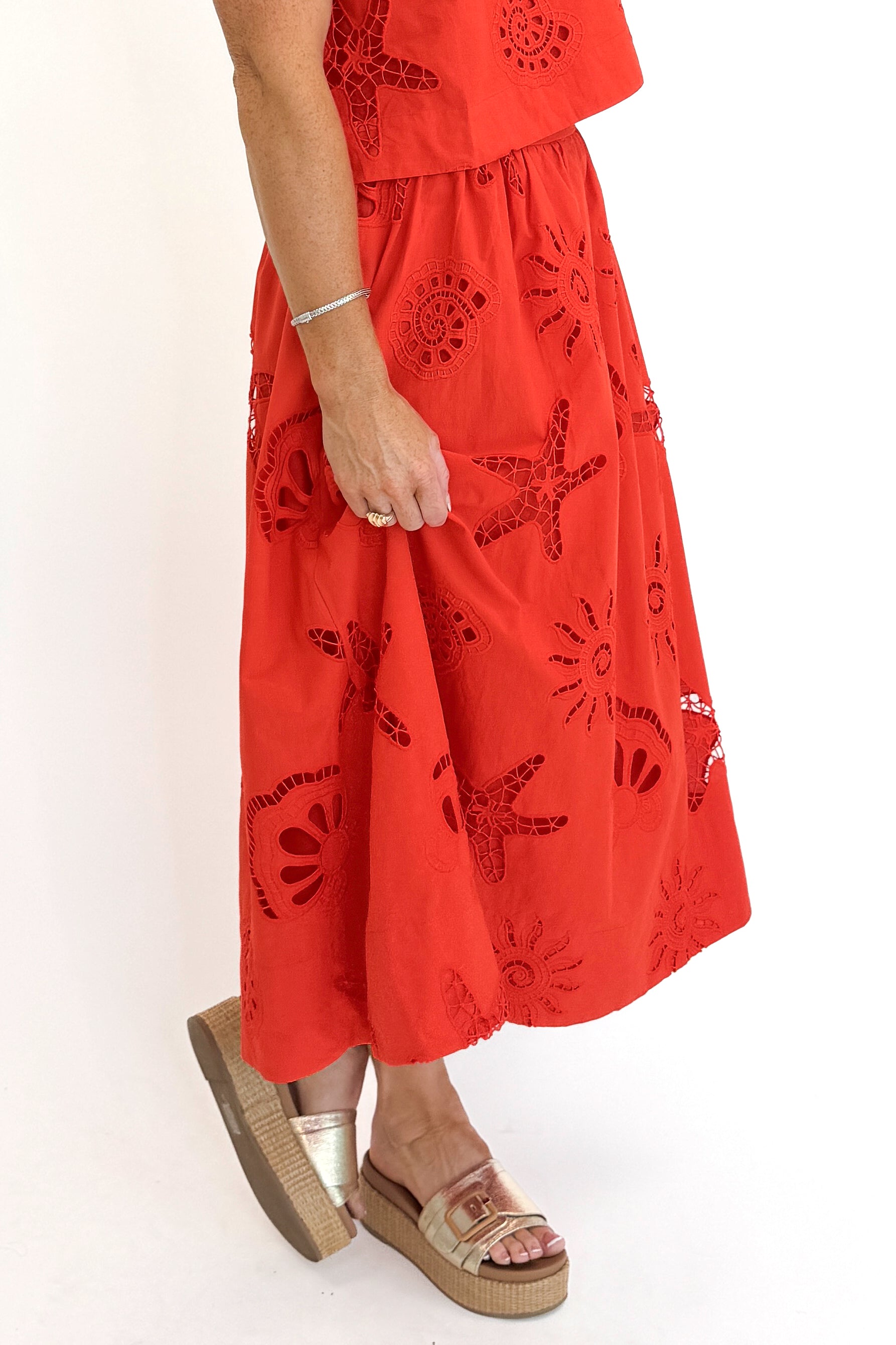 Side detail view of woman wearing Swagger Boutiqueβs Coral Shell Embroidered Tank with matching Coral Shell Embroidered Midi Skirt against white studio background.