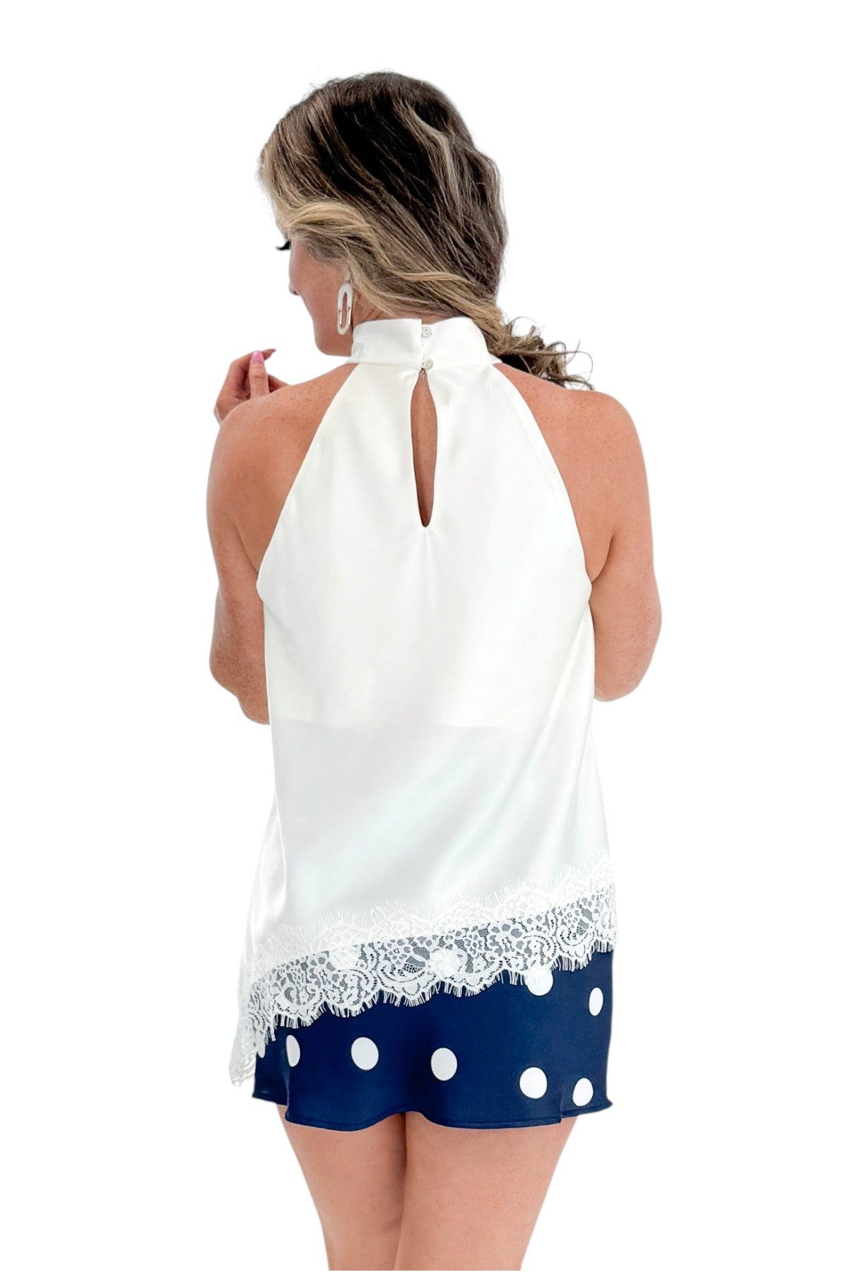 Back view of woman wearing Swagger Boutiqueβs Cream Asymmetrical Halter Neck Satin Lace Top with polka dot skirt against white studio background.
