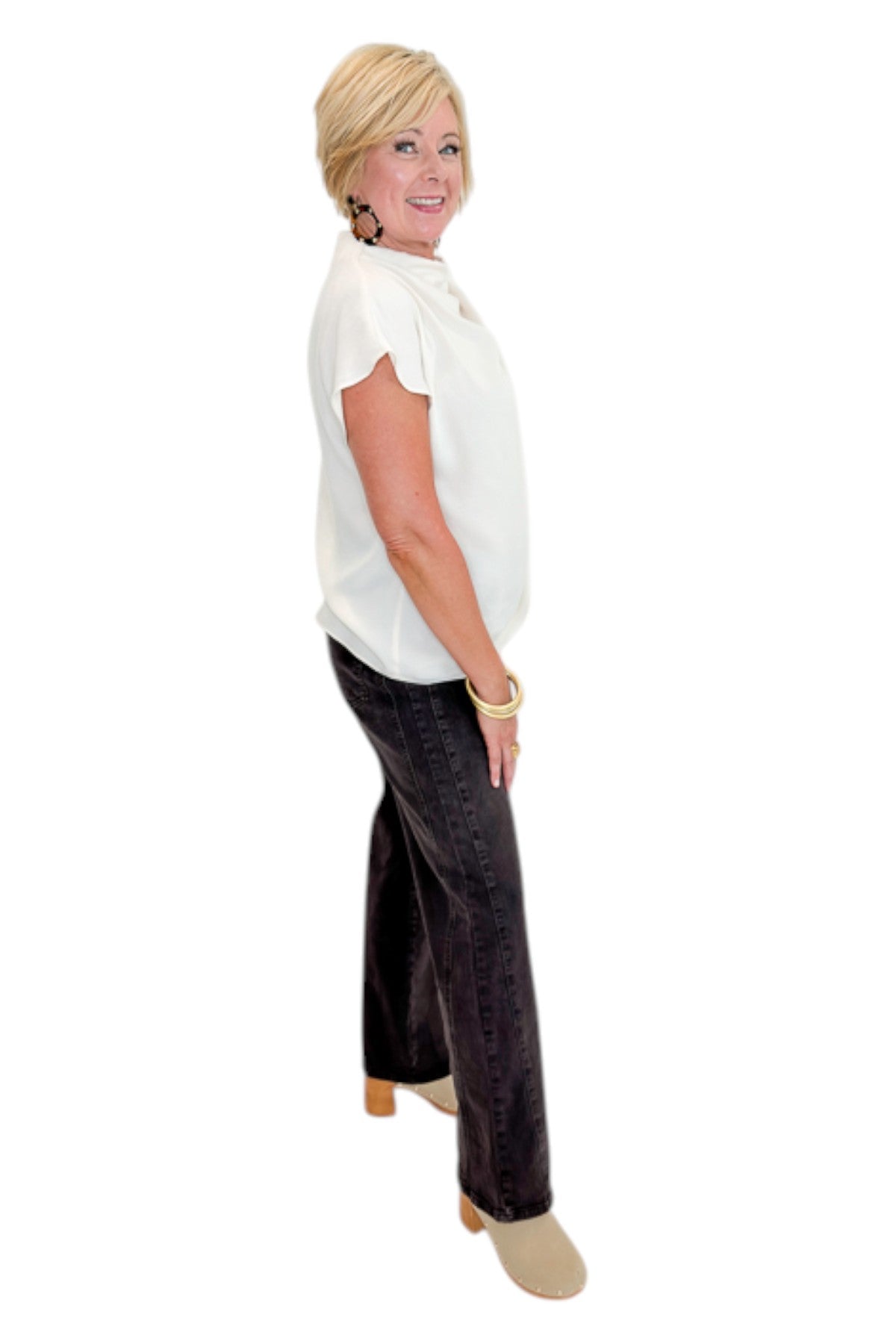 Side view of woman wearing Swagger Boutiqueās Cream Cowl Neck Top with jeans against white studio background.