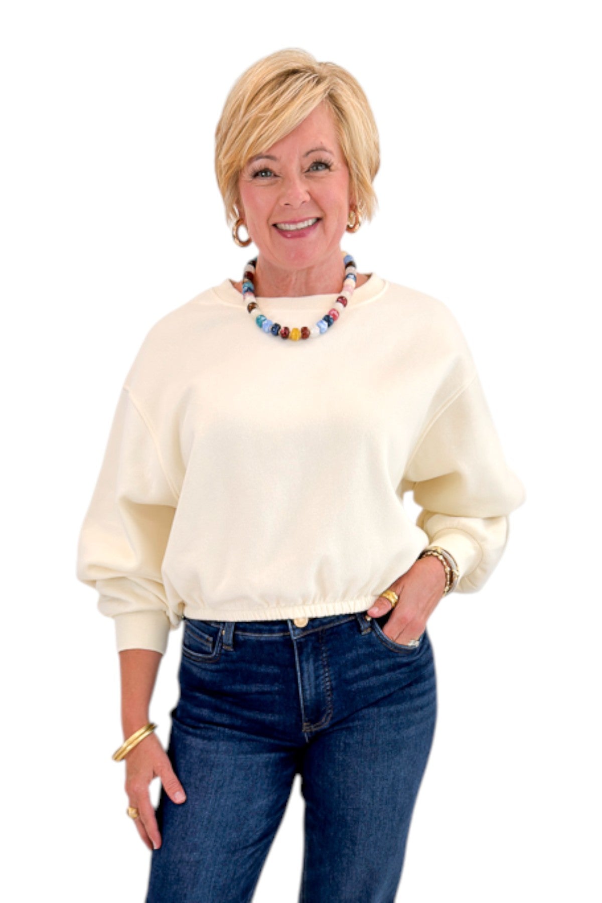 Front view of woman wearing Swagger Boutiqueās Cream Elastic Hem Sweatshirt with jeans against white studio background.