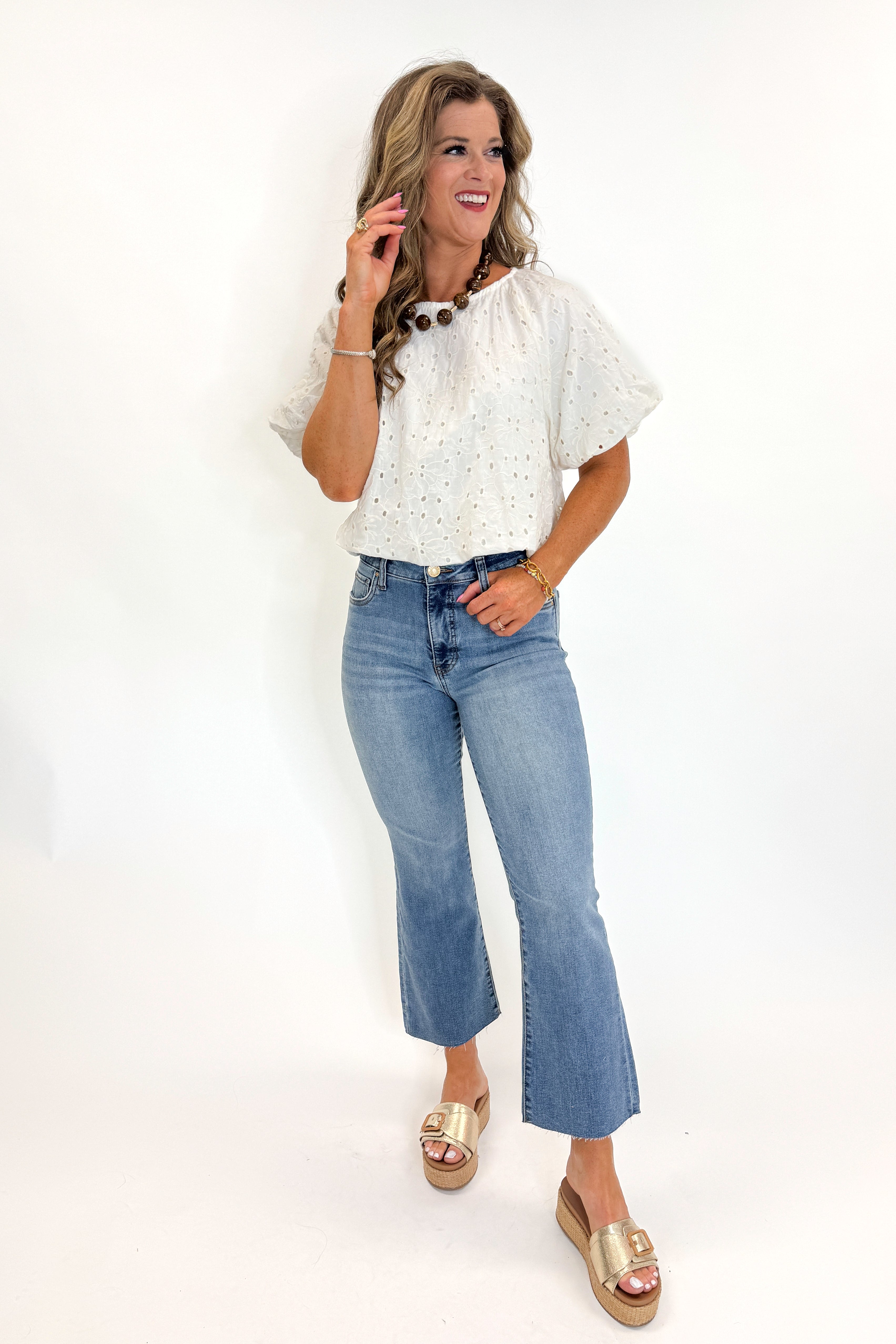 Front view of woman wearing Swagger Boutiqueβs Cream Eyelet Bubble Hem Top with jeans against white studio background.