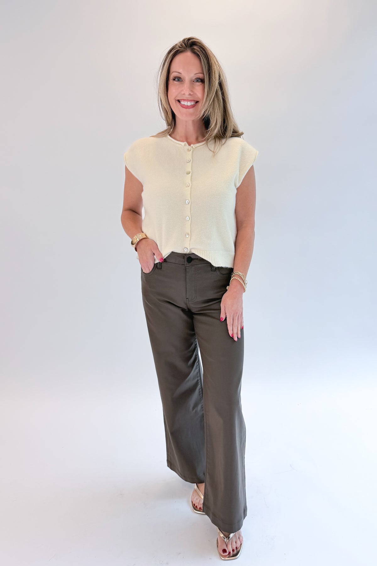 Front view of woman wearing Swagger Boutique’s Cream Sleeveless Button Up Sweater with Jeans against white studio background.