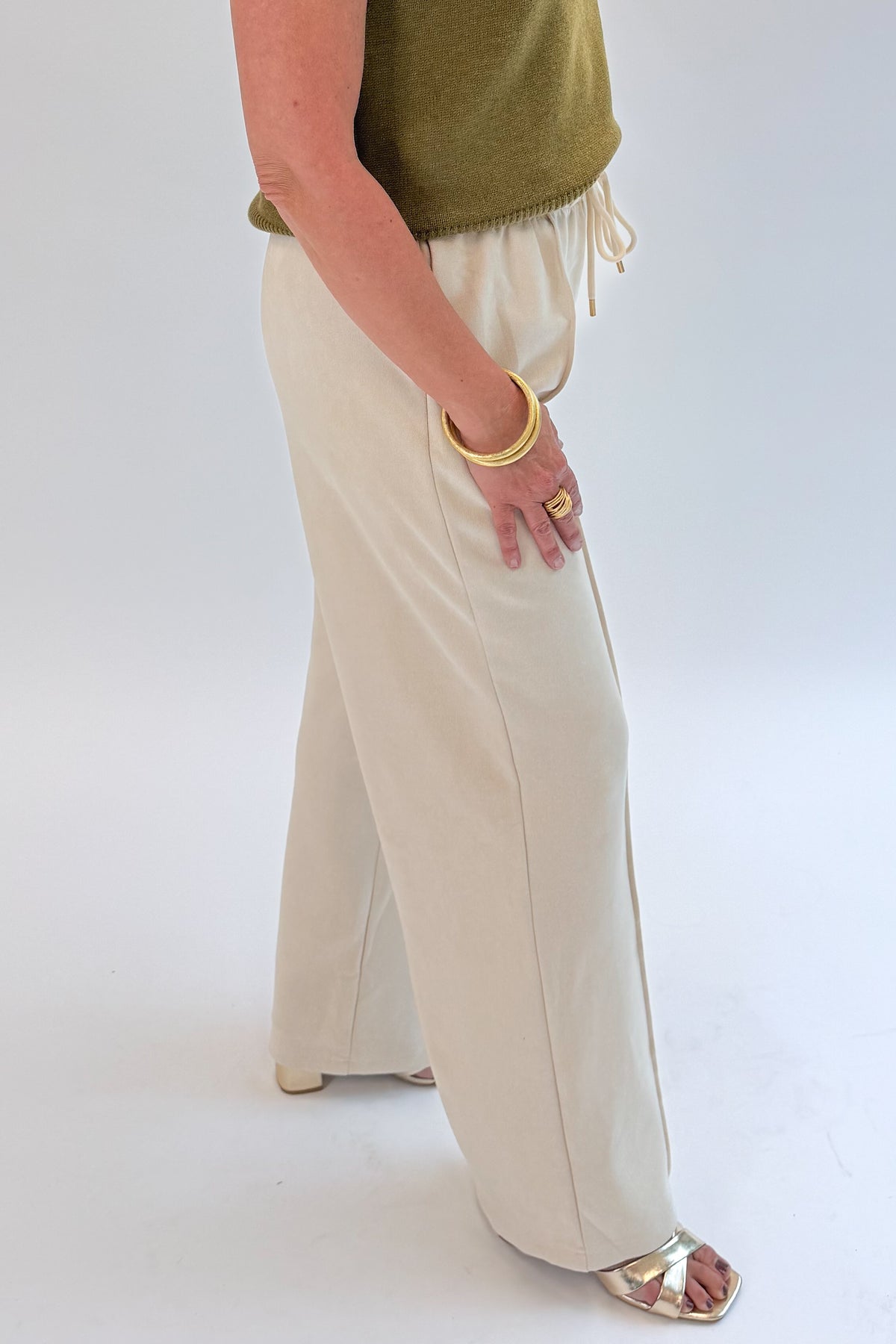 Side detail view of woman wearing Swagger Boutique’s Cream Suede Pants with sweater against white studio background.