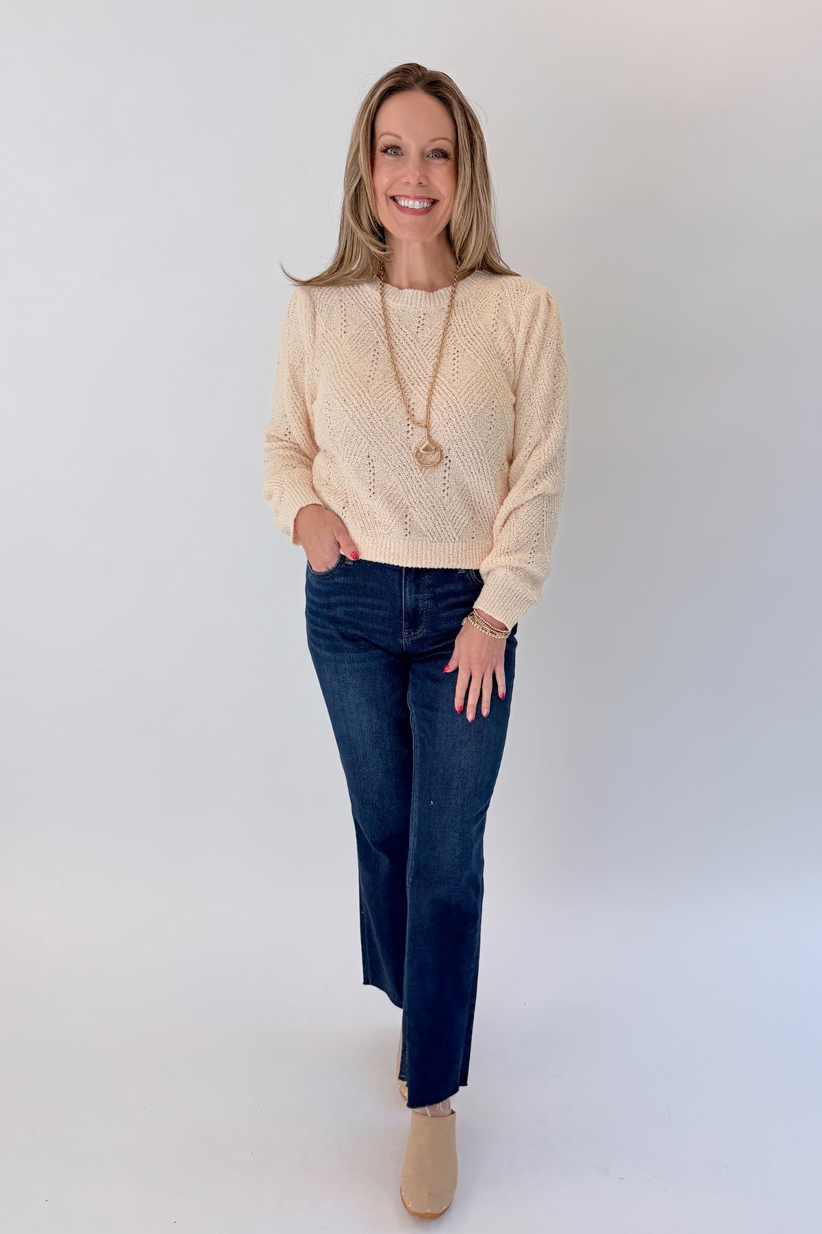 Front view of woman wearing Swagger Boutique’s Cream Textured Crew Neck Sweater with jeans against white studio background.