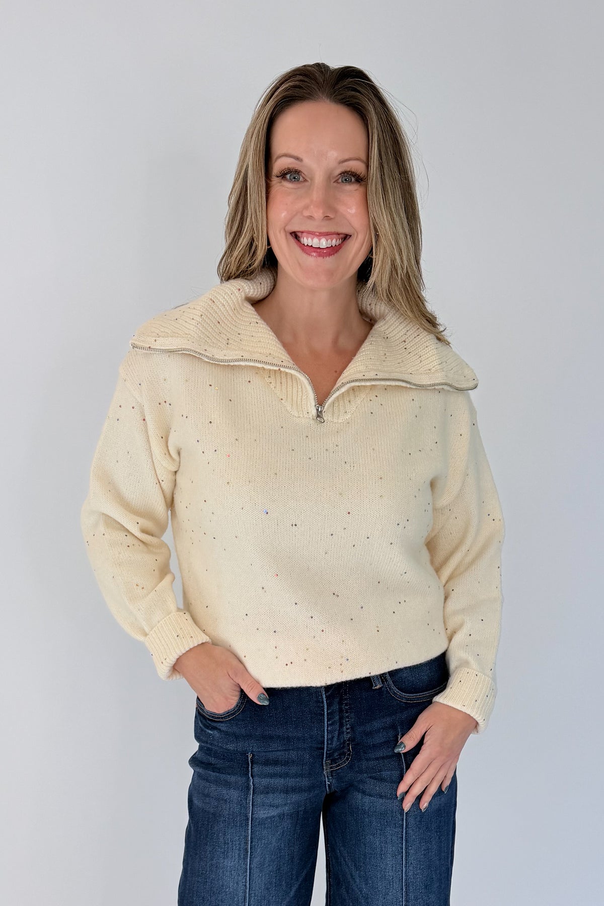 Front view of woman wearing Swagger Boutique’s Cream With Multi Sequins Sweater with jeans against white studio background.