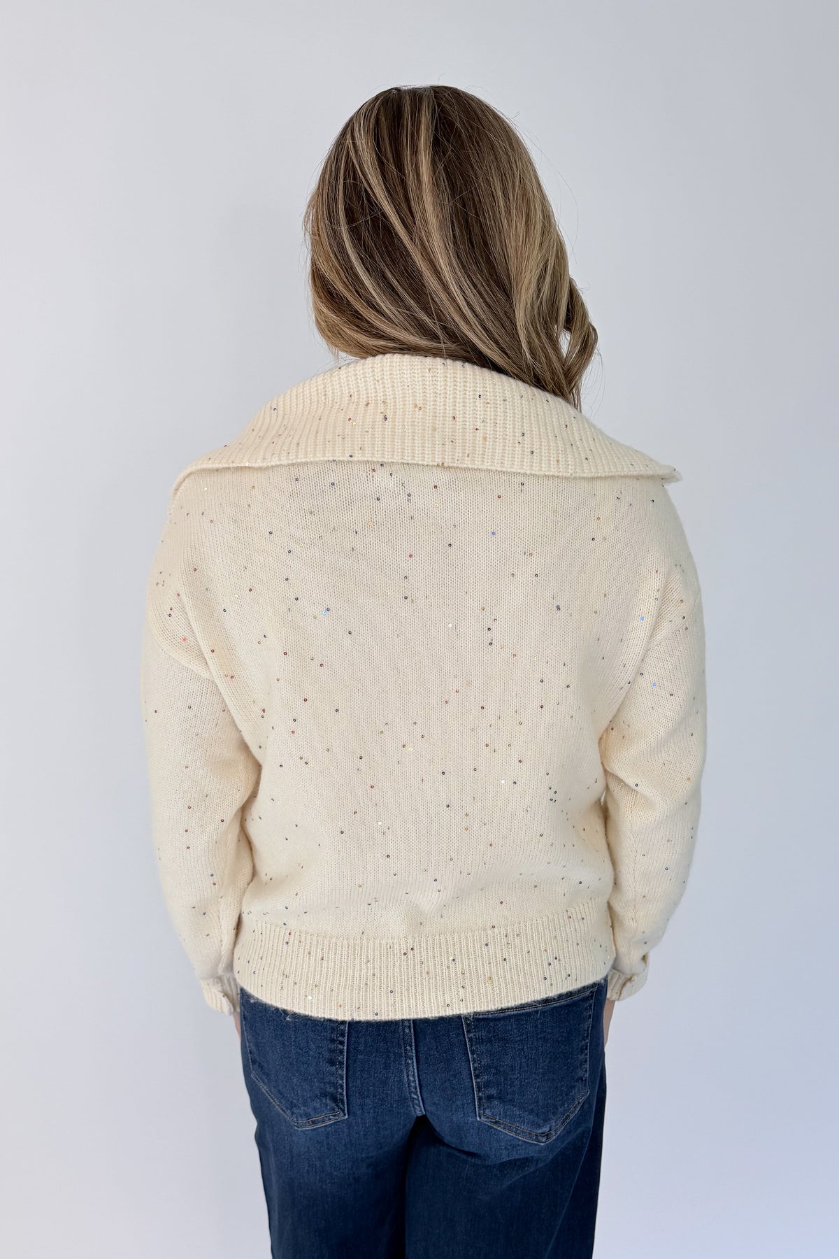 Back view of woman wearing Swagger Boutique’s Cream With Multi Sequins Sweater with jeans against white studio background.