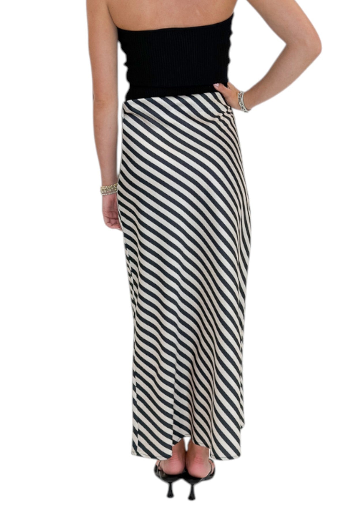 Back view of woman wearing Swagger Boutique’s Cream & Black Striped Satin Midi Skirt with black top against white studio background.