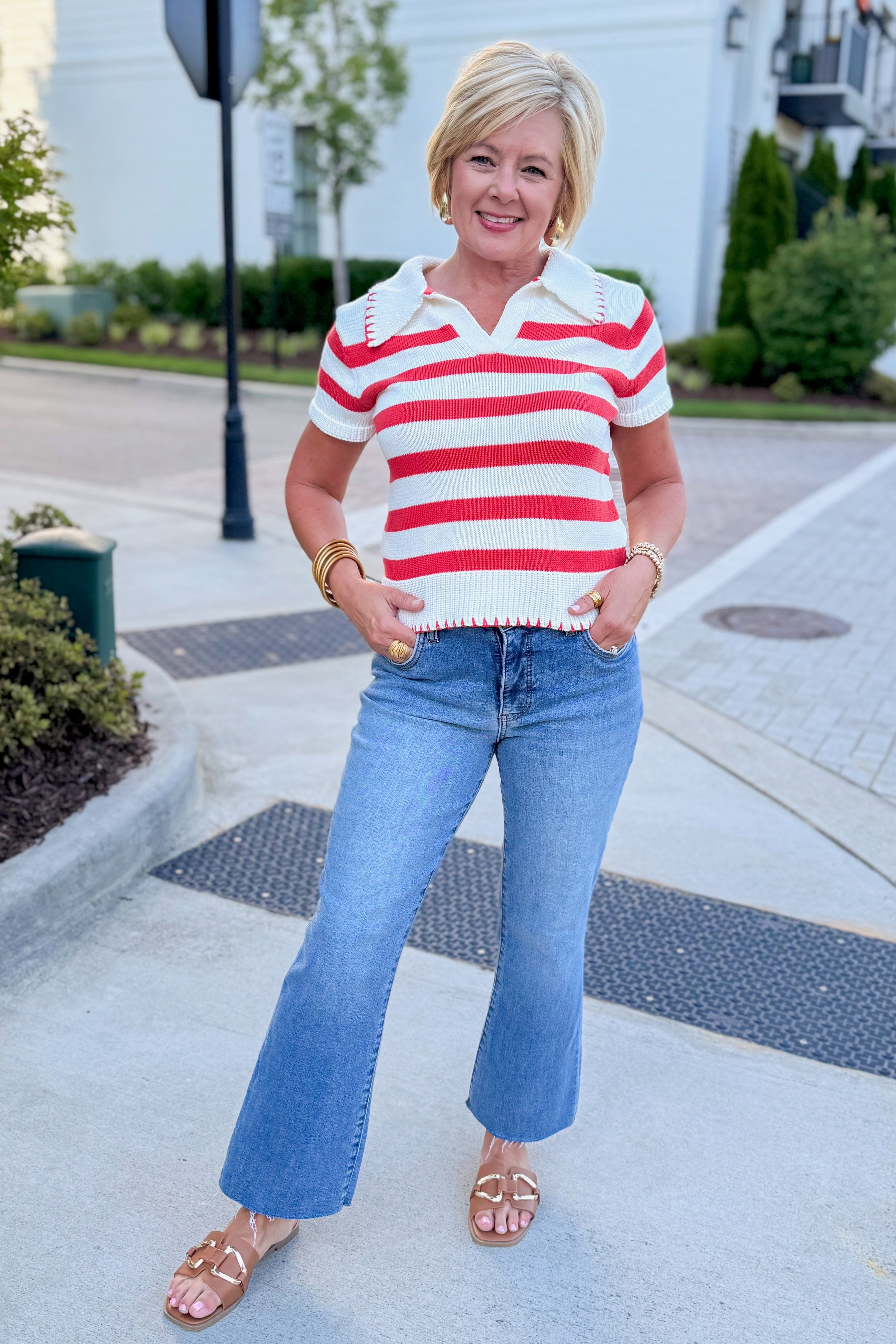 Front view of woman wearing Swagger Boutiqueβs Cream & Coral Striped Knit Top with jeans walking outside at a city.