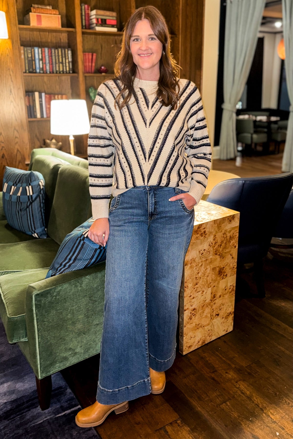 Front view of woman wearing Swagger Boutique’s Cream & Navy Chevron Sweater with jeans standing in a lounge.