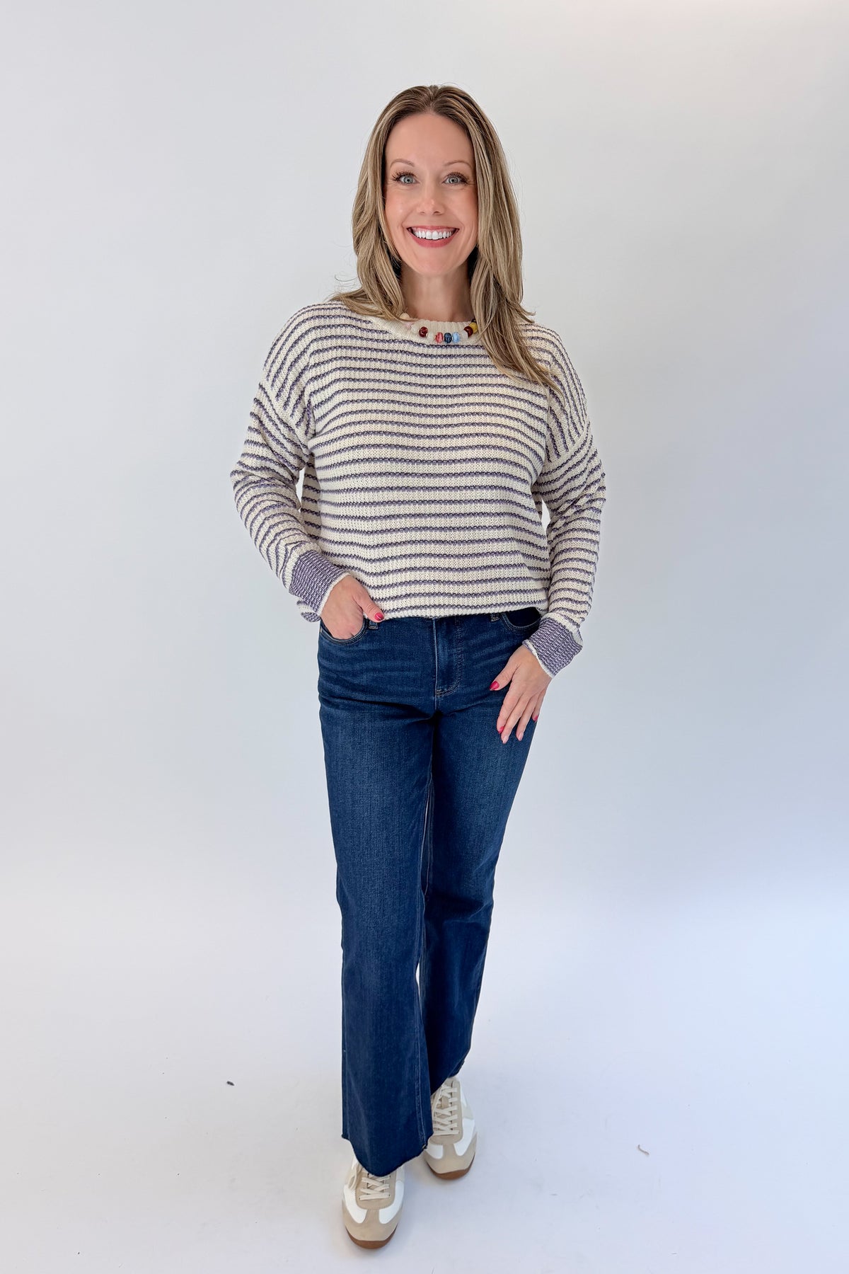Front view of woman wearing Swagger Boutique’s Cream & Purple Striped Sweater with jeans against white studio background.