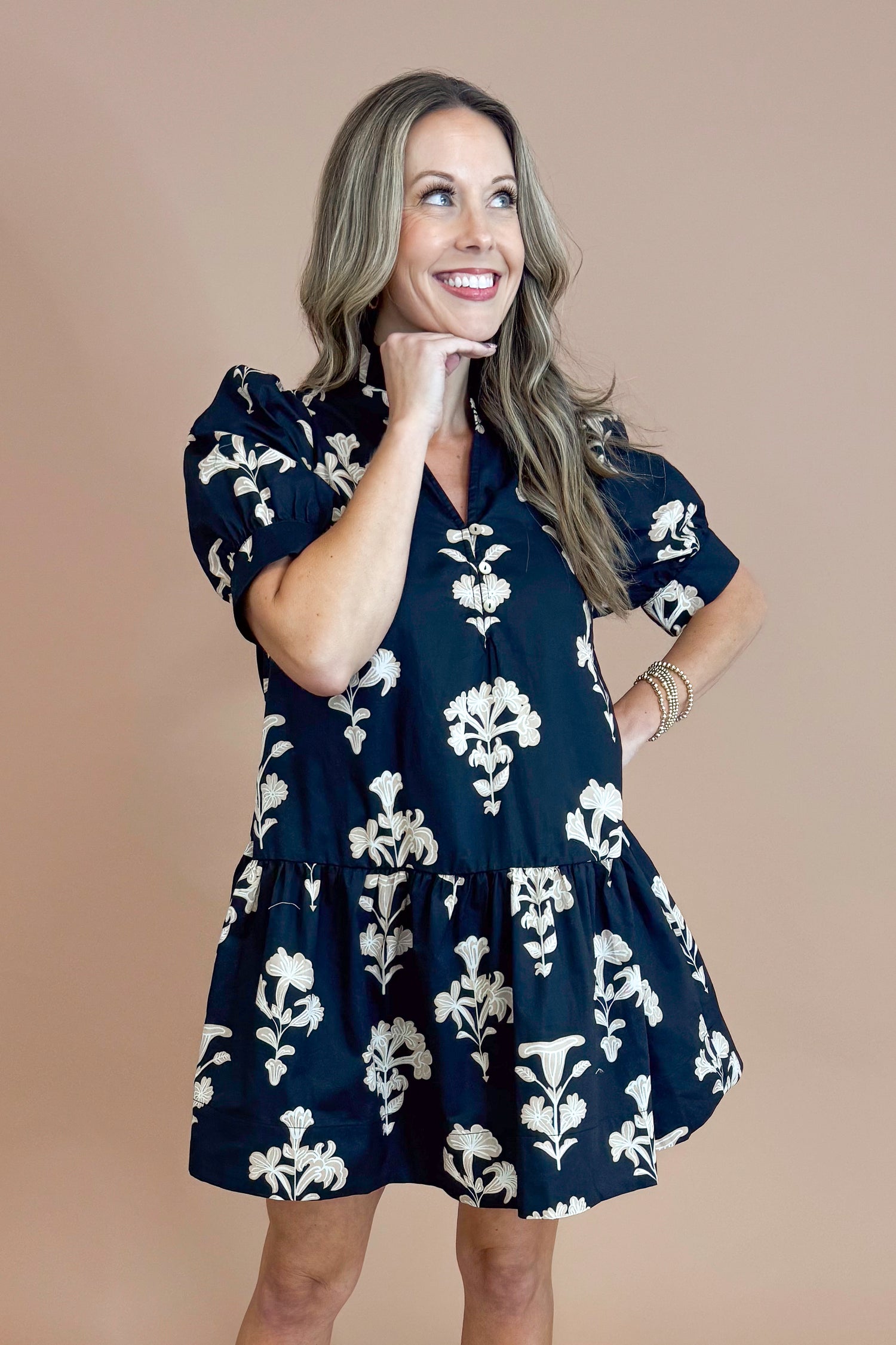 Woman wearing a navy dress with white floral pattern against a beige background
