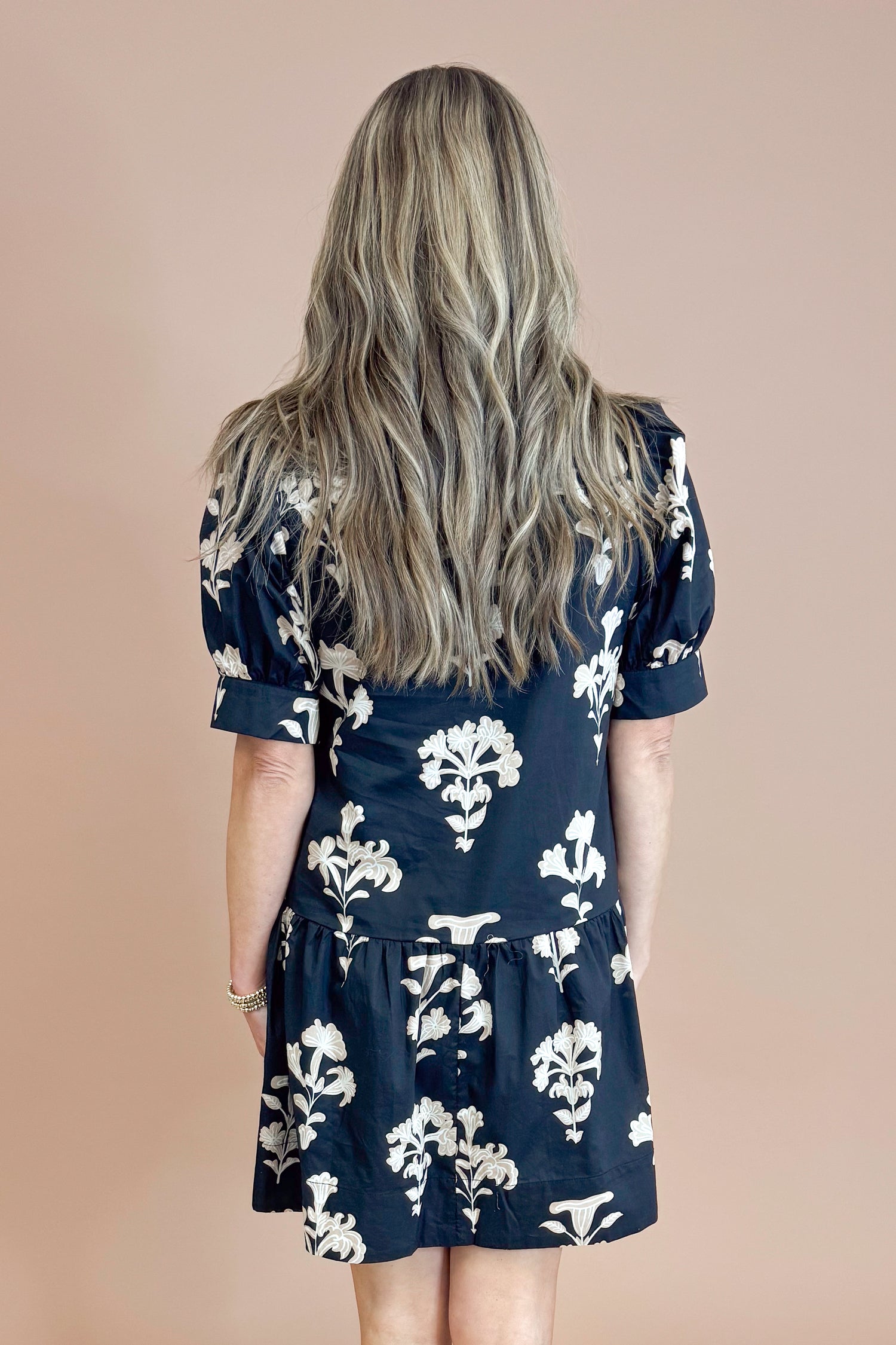 Person wearing a navy dress with white floral pattern from behind on a beige background