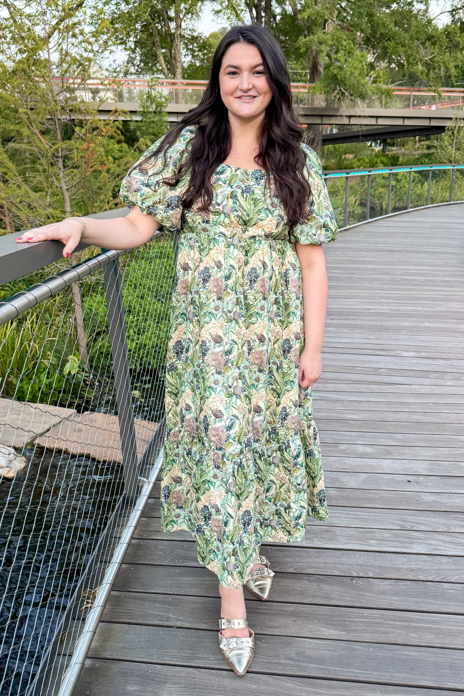 Woman in a floral dress standing on a wooden bridge with greenery in the background