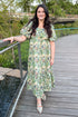 Woman in a floral dress standing on a wooden bridge with greenery in the background
