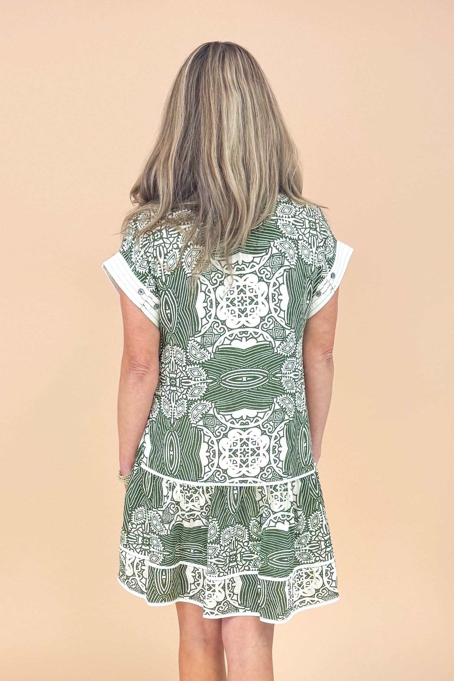 Woman wearing a green and white patterned dress against a beige background