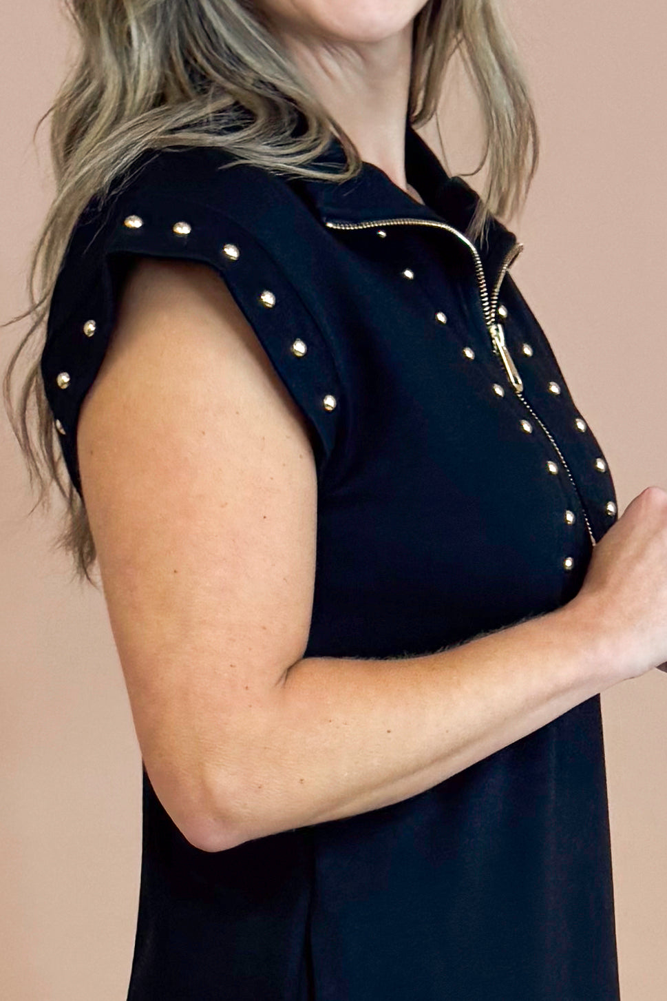 Black sleeveless top with gold embellishments on a beige background
